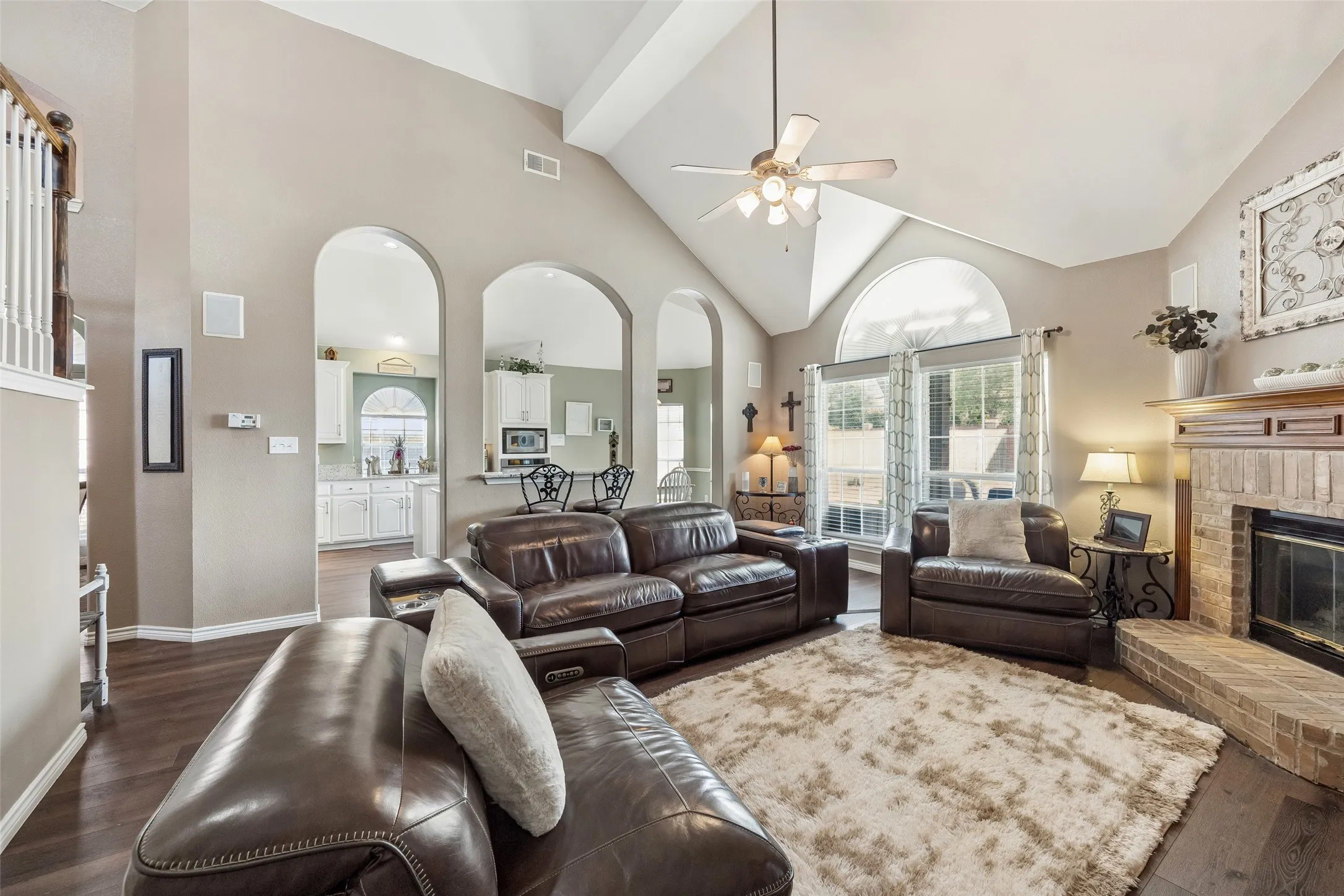 Natural Light Meets a Classic Fireplace — A wall of windows topped by an oversized arched transom brings abundant daylight into the family room, while the brick fireplace and raised hearth create a natural anchor for the room.