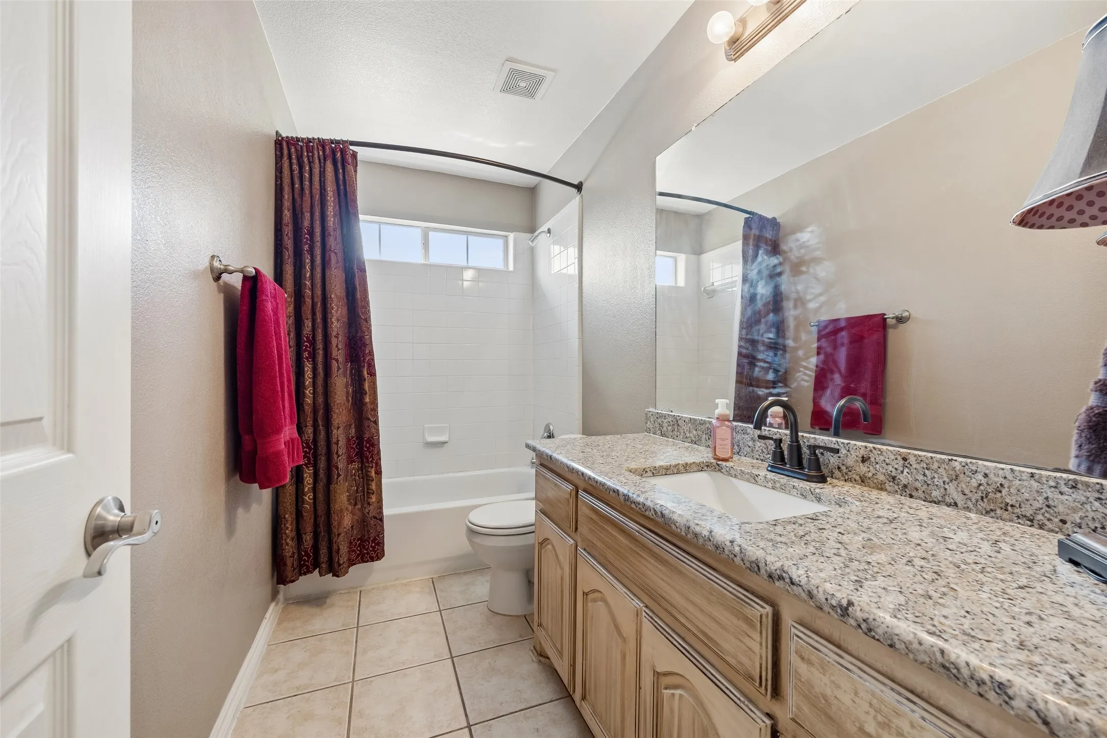 Secondary Full Bath — The upstairs bath includes a granite-topped vanity with generous counter space, a tub-shower combination, tile flooring, and a large wall mirror.