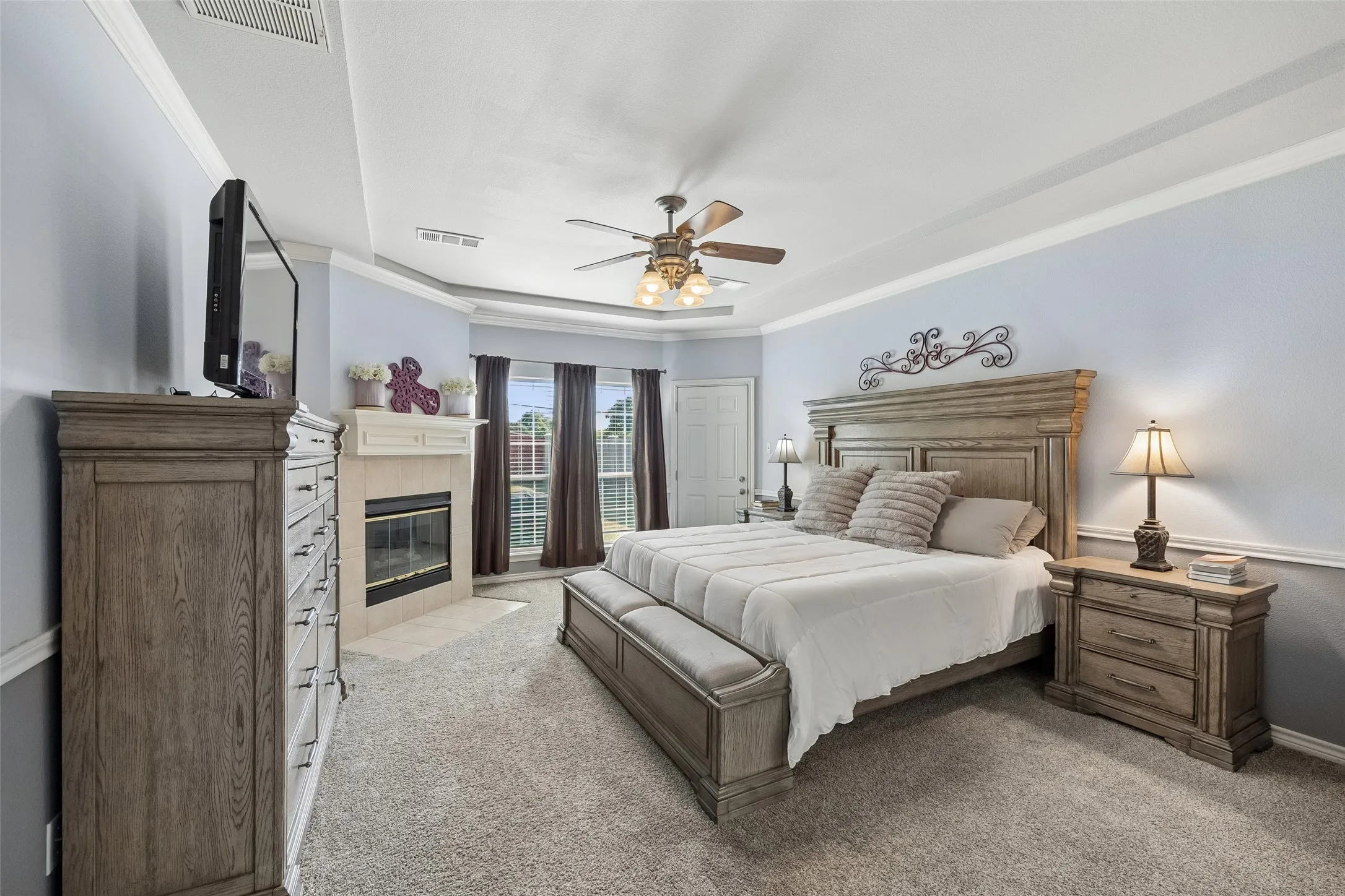 Primary Suite with Its Own Fireplace — The spacious primary bedroom offers more than just room for a large furniture arrangement. A corner fireplace, tray ceiling with crown molding, and backyard-facing windows give the suite several features not commonly found together.