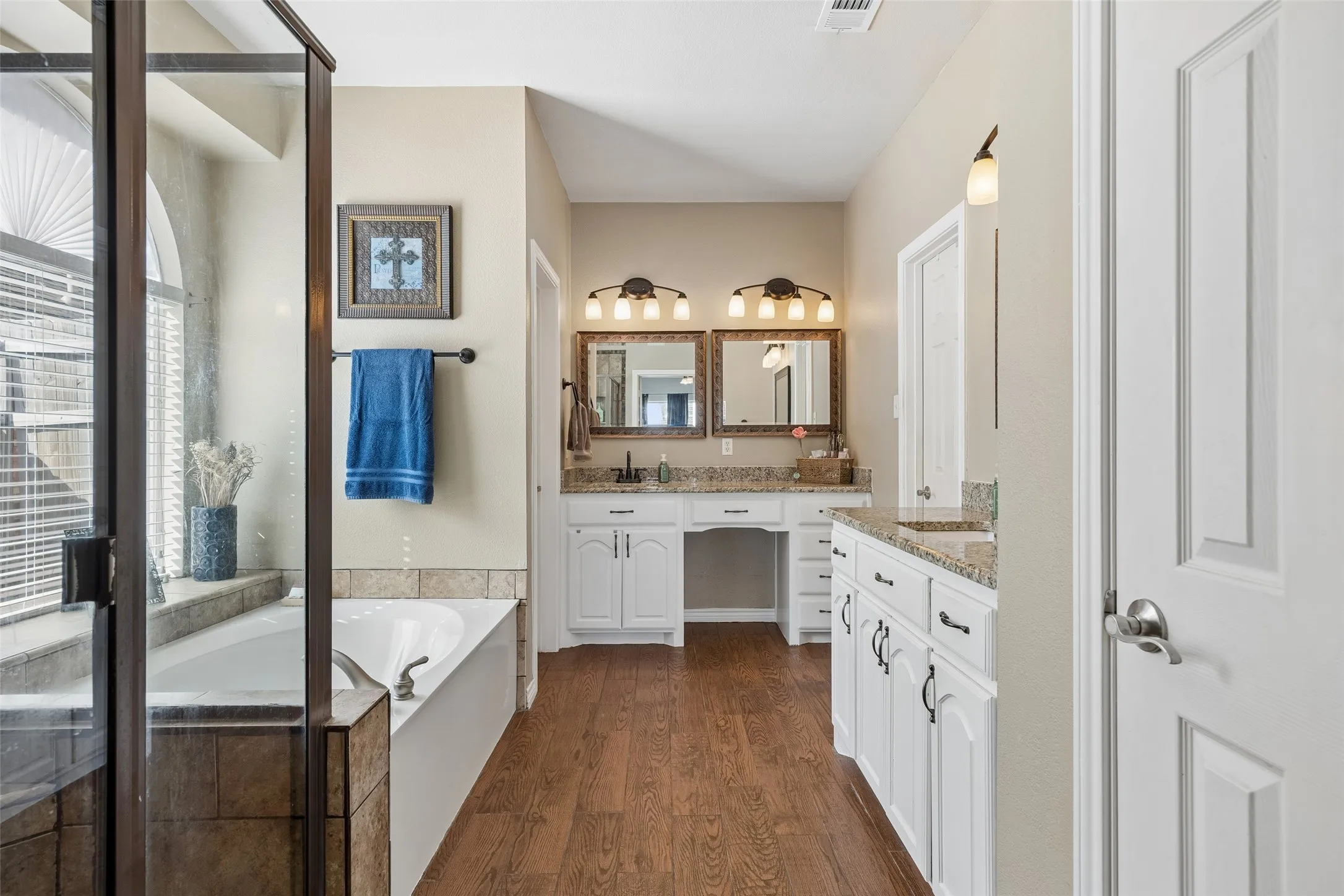 Primary Bath with Separate Grooming Areas — The primary bath offers two separate vanity areas rather than a single shared counter. Granite countertops, extensive cabinetry, and a dedicated seated grooming space provide useful storage and room for everyday routines.