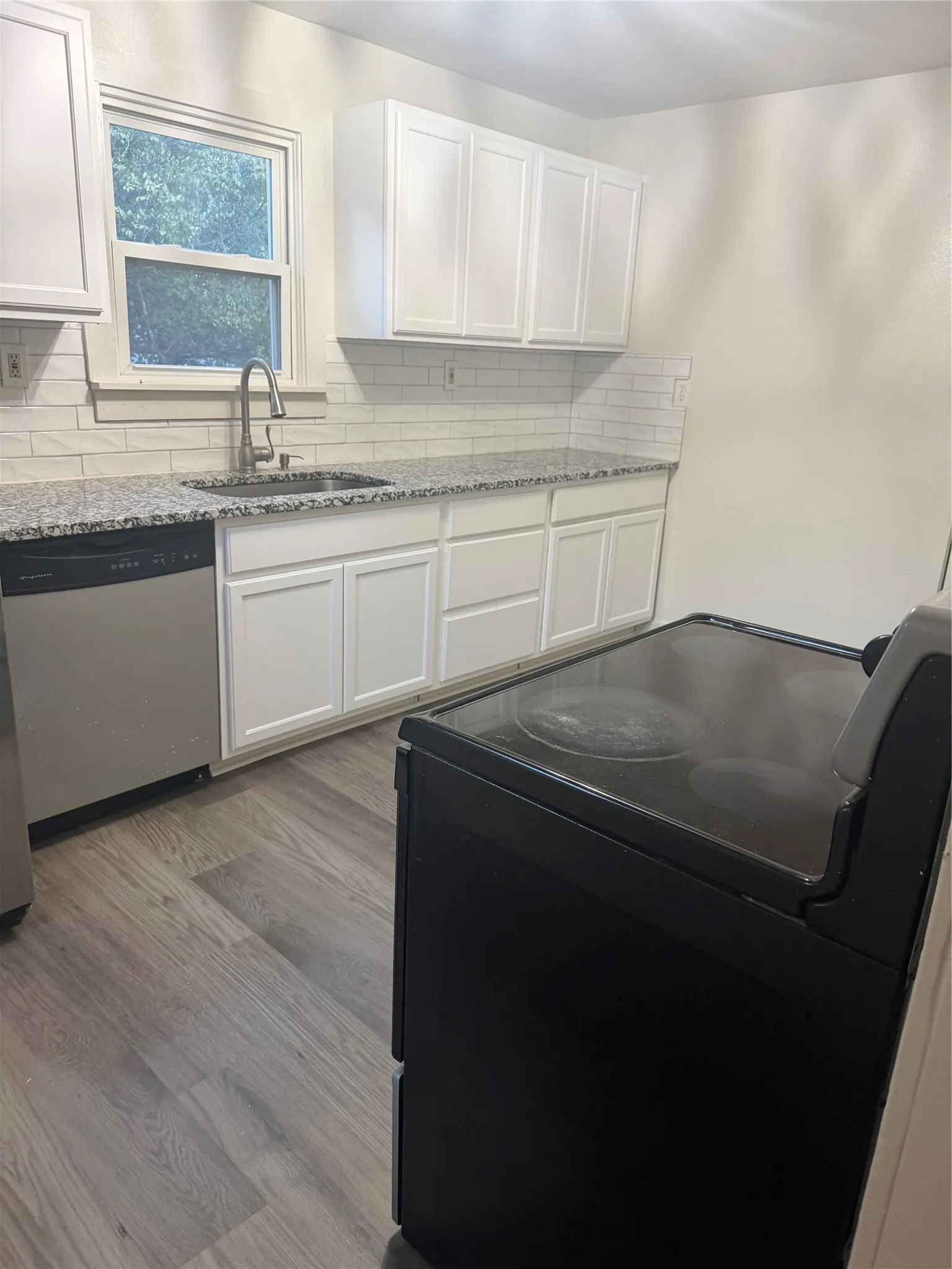 Kitchen featuring white shaker cabinetry, speckled countertops, subway tile backsplash, stainless steel sink, and wood-finish flooring