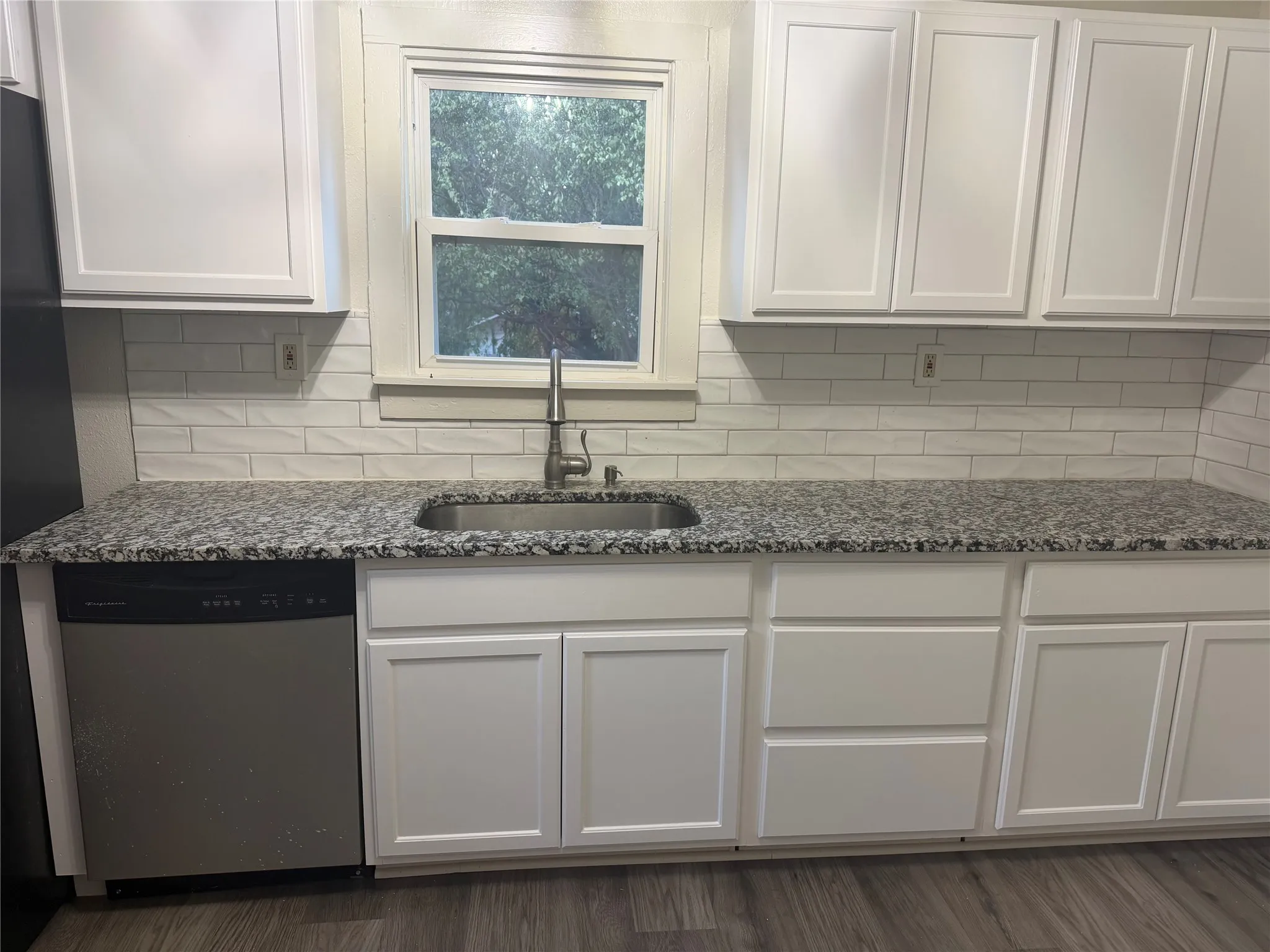 White shaker-style cabinetry, granite countertops, subway tile backsplash, stainless steel sink with a gooseneck faucet, and wood-finish flooring