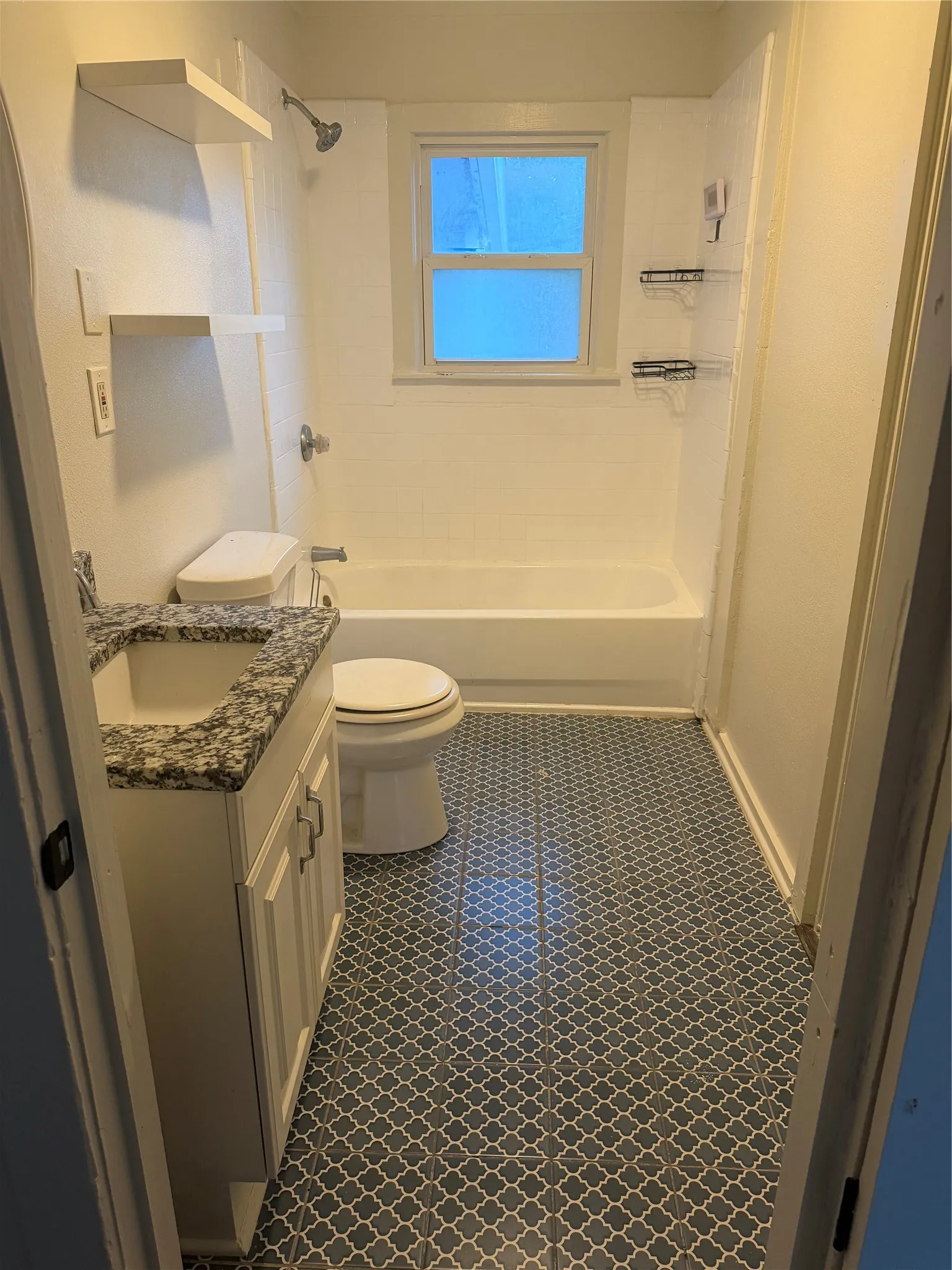 Bathroom featuring a white vanity with a granite-style countertop, decorative floor tiling, a single window, and a shower-tub combination