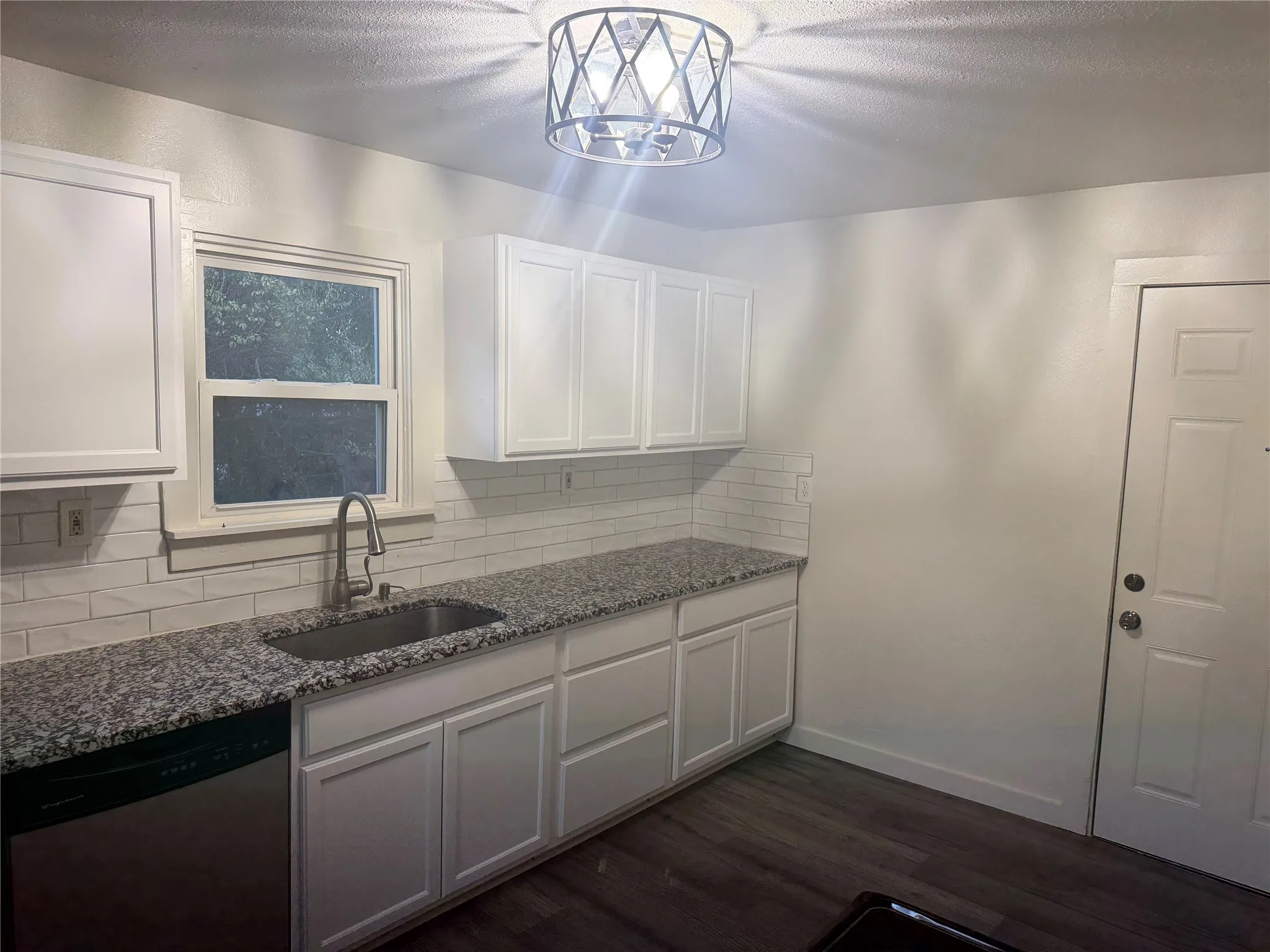 White shaker-style cabinetry, granite countertops, subway tile backsplash, stainless steel sink, and wood-finish flooring
