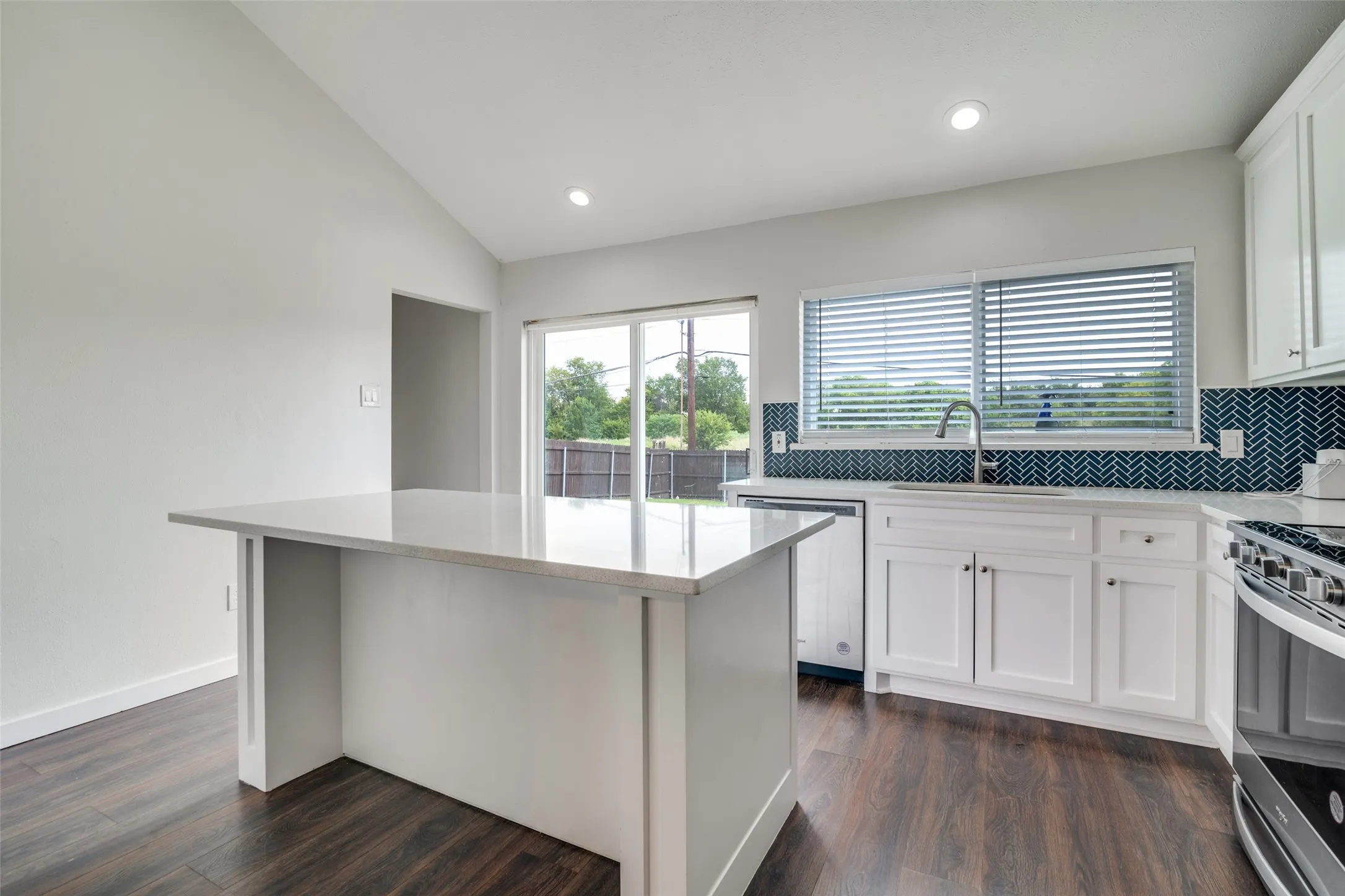 Kitchen with white cabinets, decorative backsplash, vaulted ceiling, light stone counters, and dark wood finished floors
