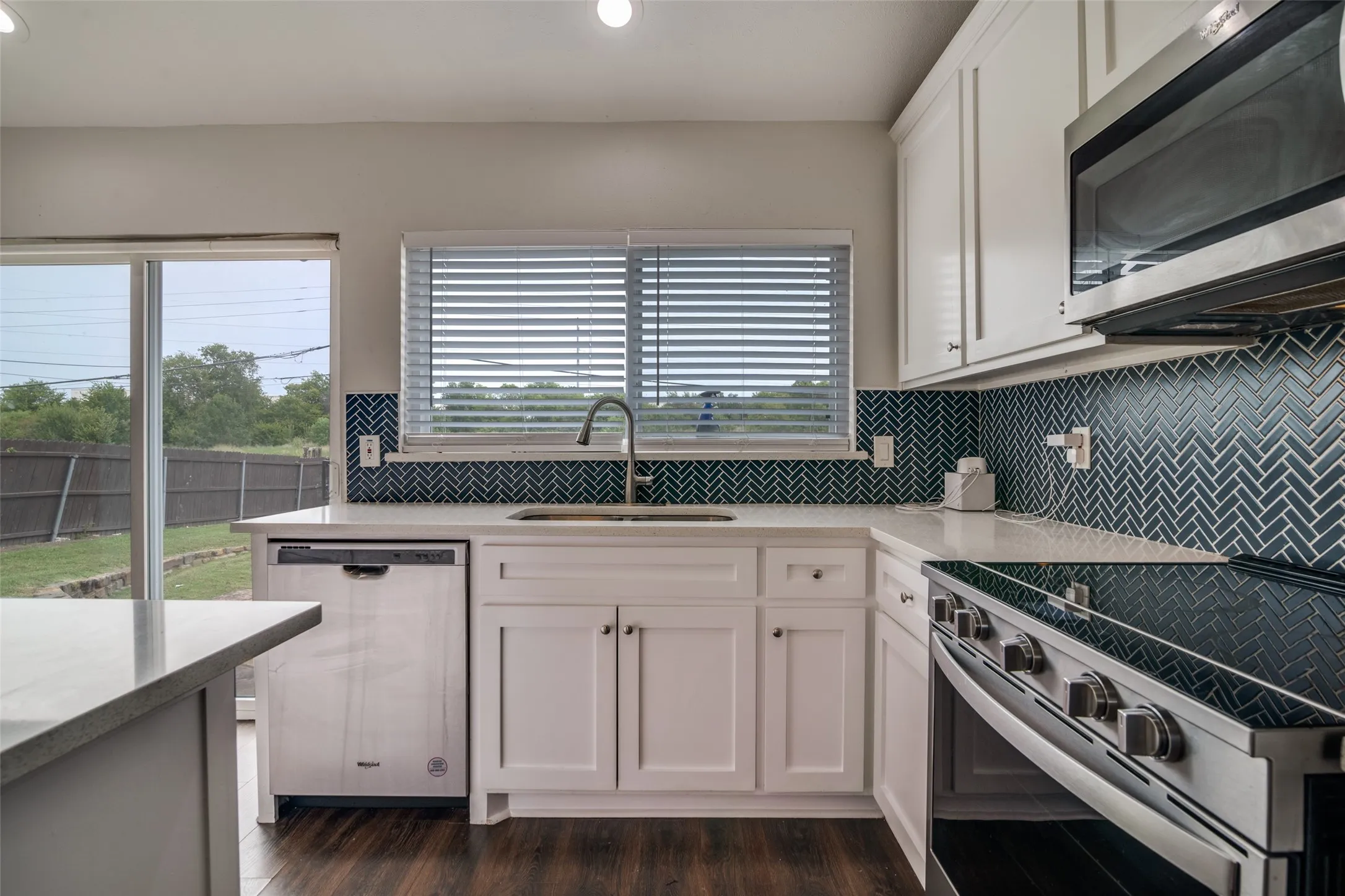 Kitchen with stainless steel appliances, light stone countertops, white cabinetry, backsplash, and recessed lighting