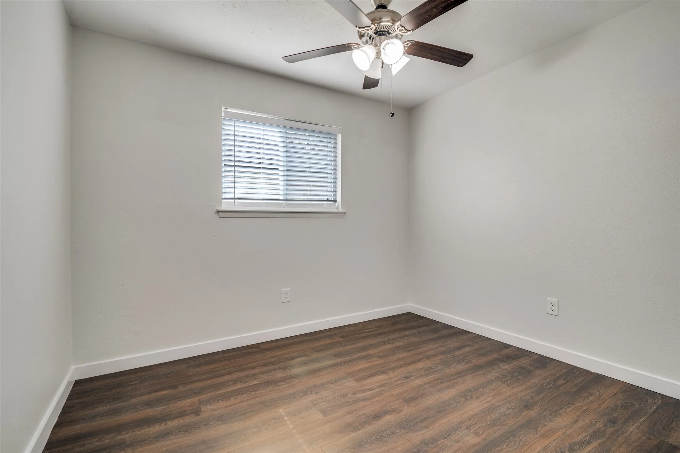 Empty room with dark wood-style floors and a ceiling fan