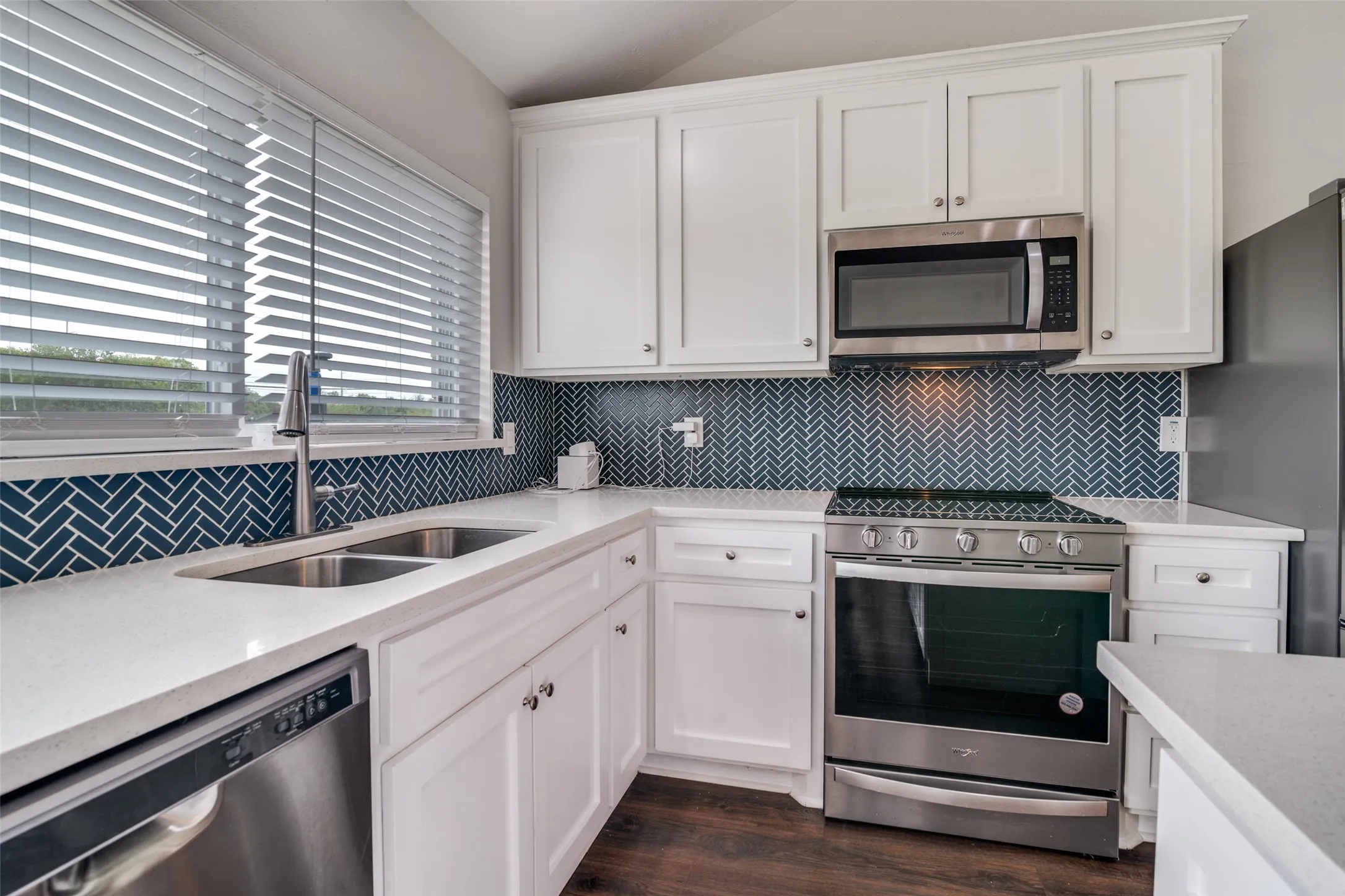 Kitchen with stainless steel appliances, tasteful backsplash, white cabinetry, light stone counters, and lofted ceiling