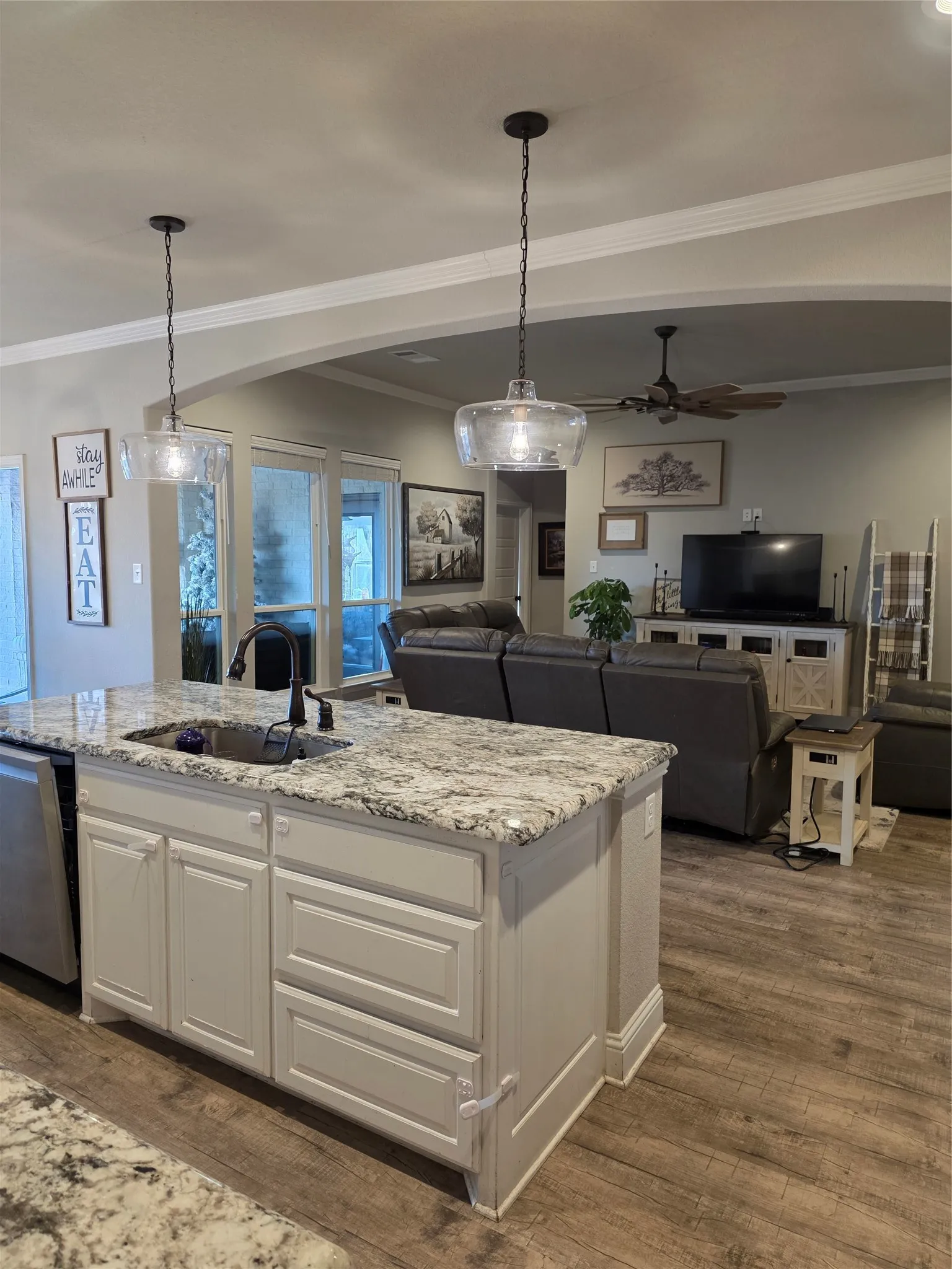Kitchen featuring white cabinetry, open floor plan, light stone counters, dark wood-style floors, and a center island with sink