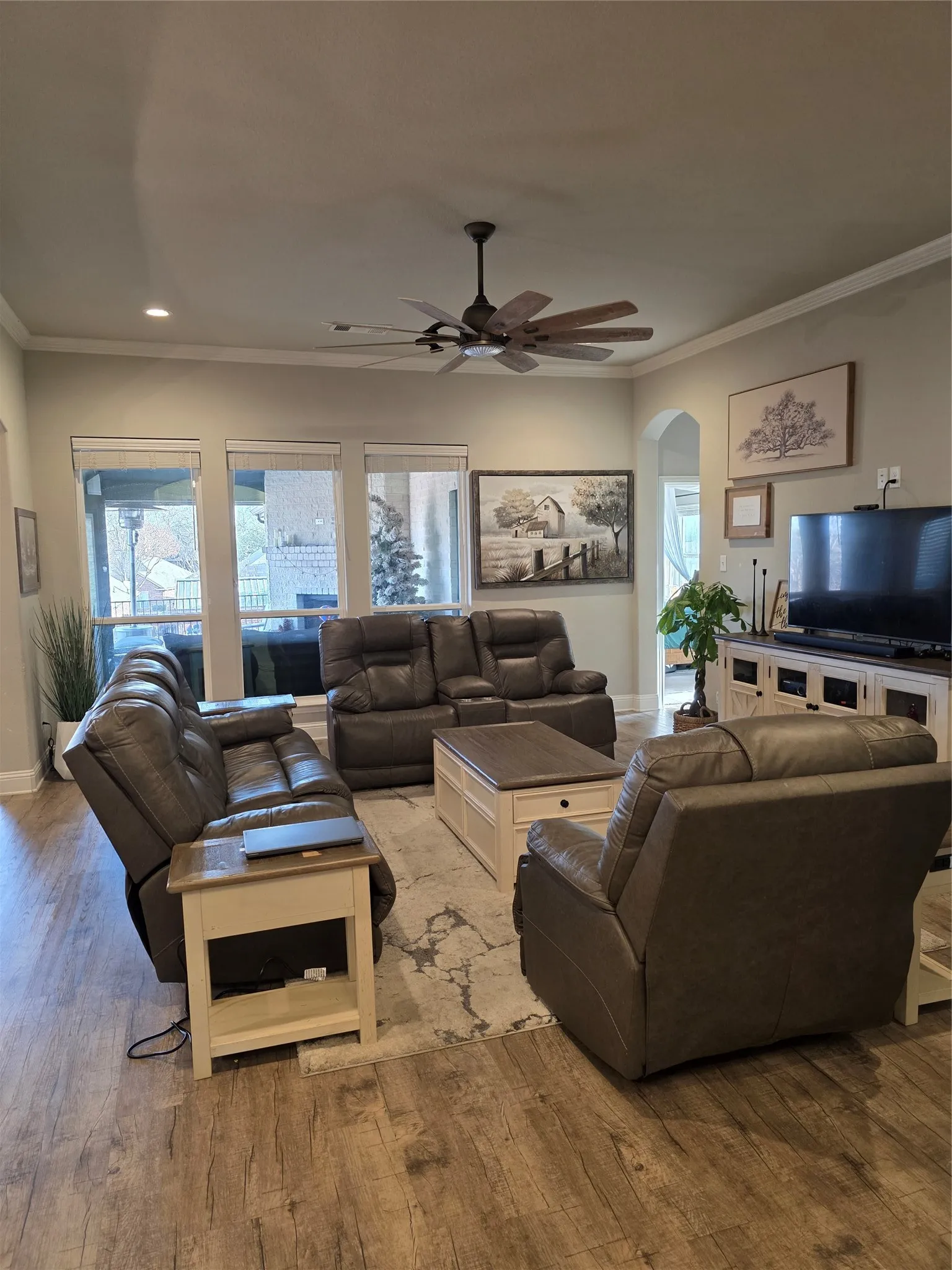Living room with arched walkways, crown molding, wood-type flooring, and a ceiling fan
