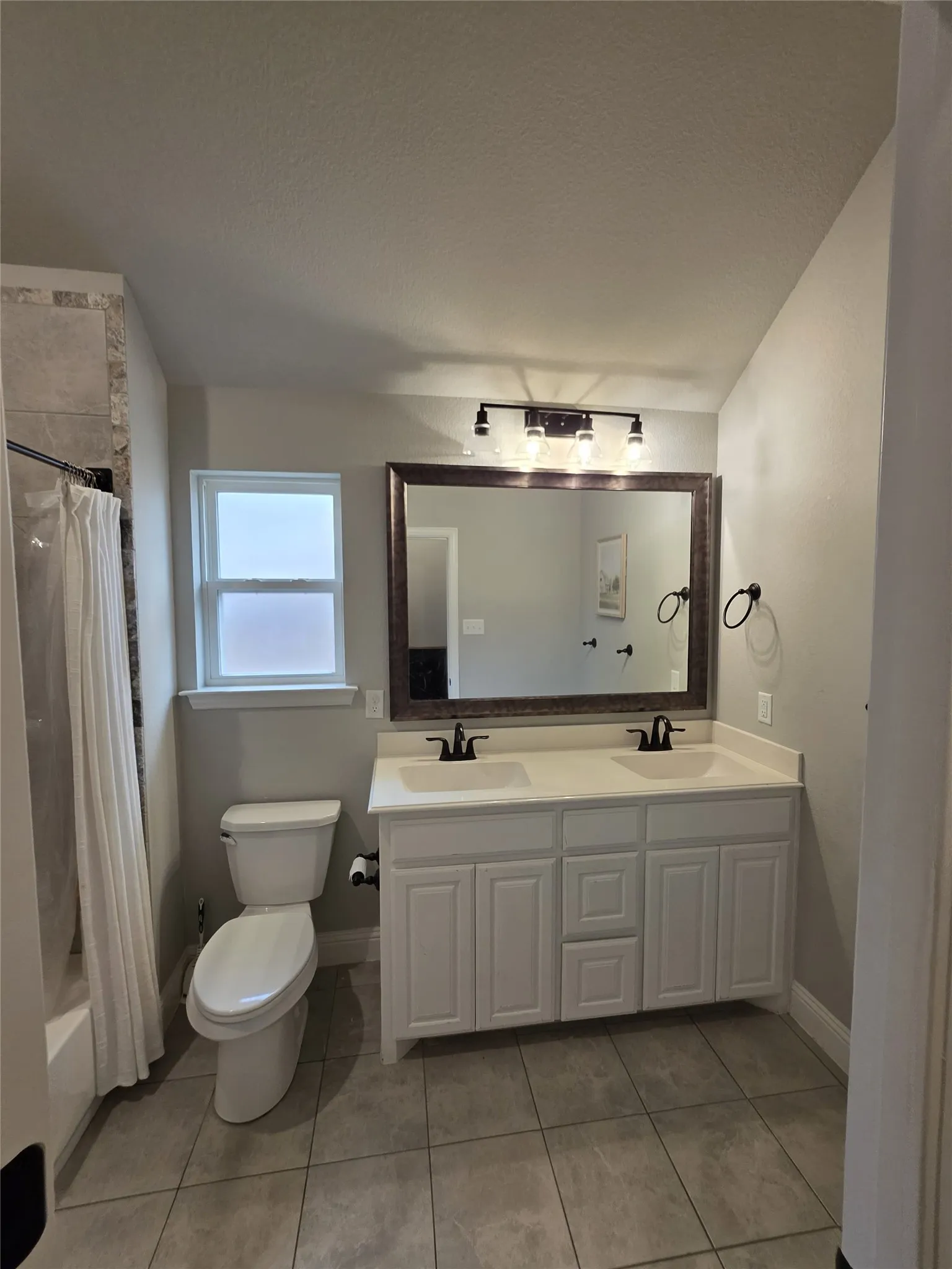 Bathroom featuring double vanity, shower / bathtub combination with curtain, and light tile patterned flooring