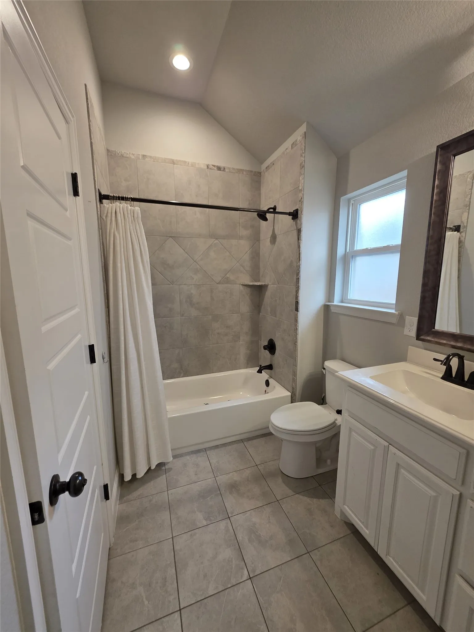 Bathroom featuring vanity, lofted ceiling, shower / bathtub combination with curtain, and light tile patterned floors