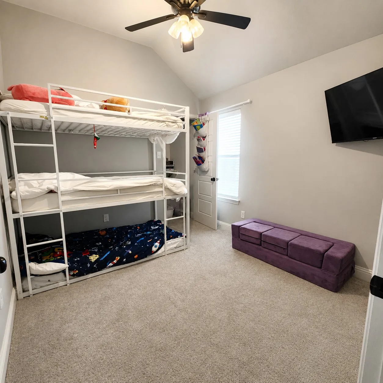Vaulted ceiling with ceiling fan, wall-mounted television, neutral carpeting, and a window with blinds