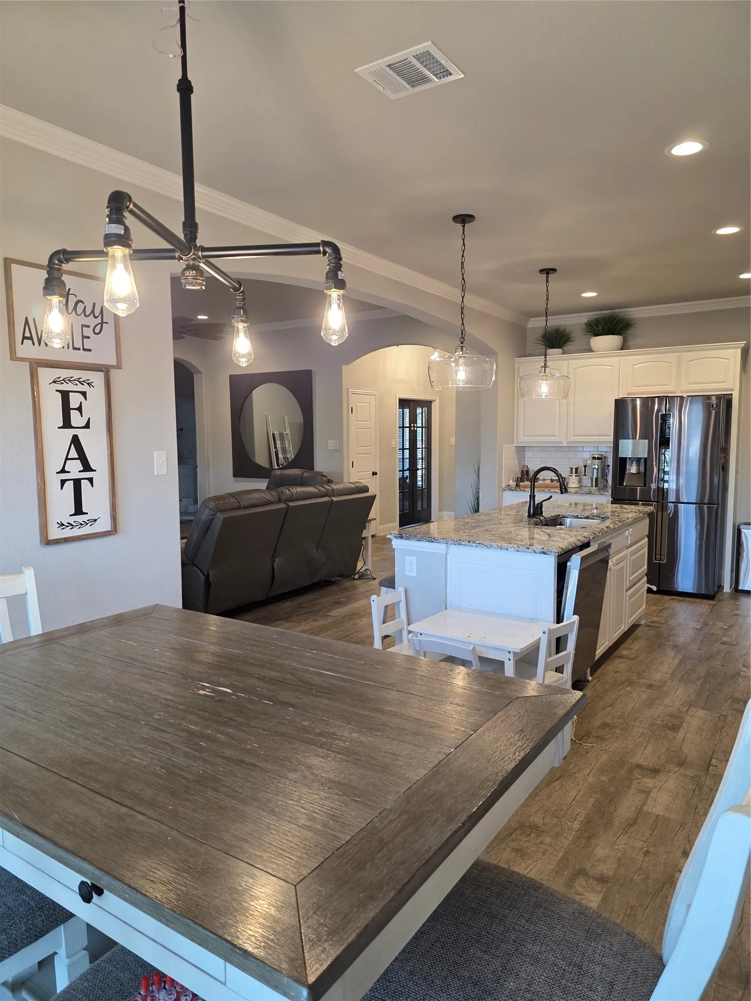 Kitchen with light stone countertops, ornamental molding, stainless steel fridge, pendant lighting, and arched walkways