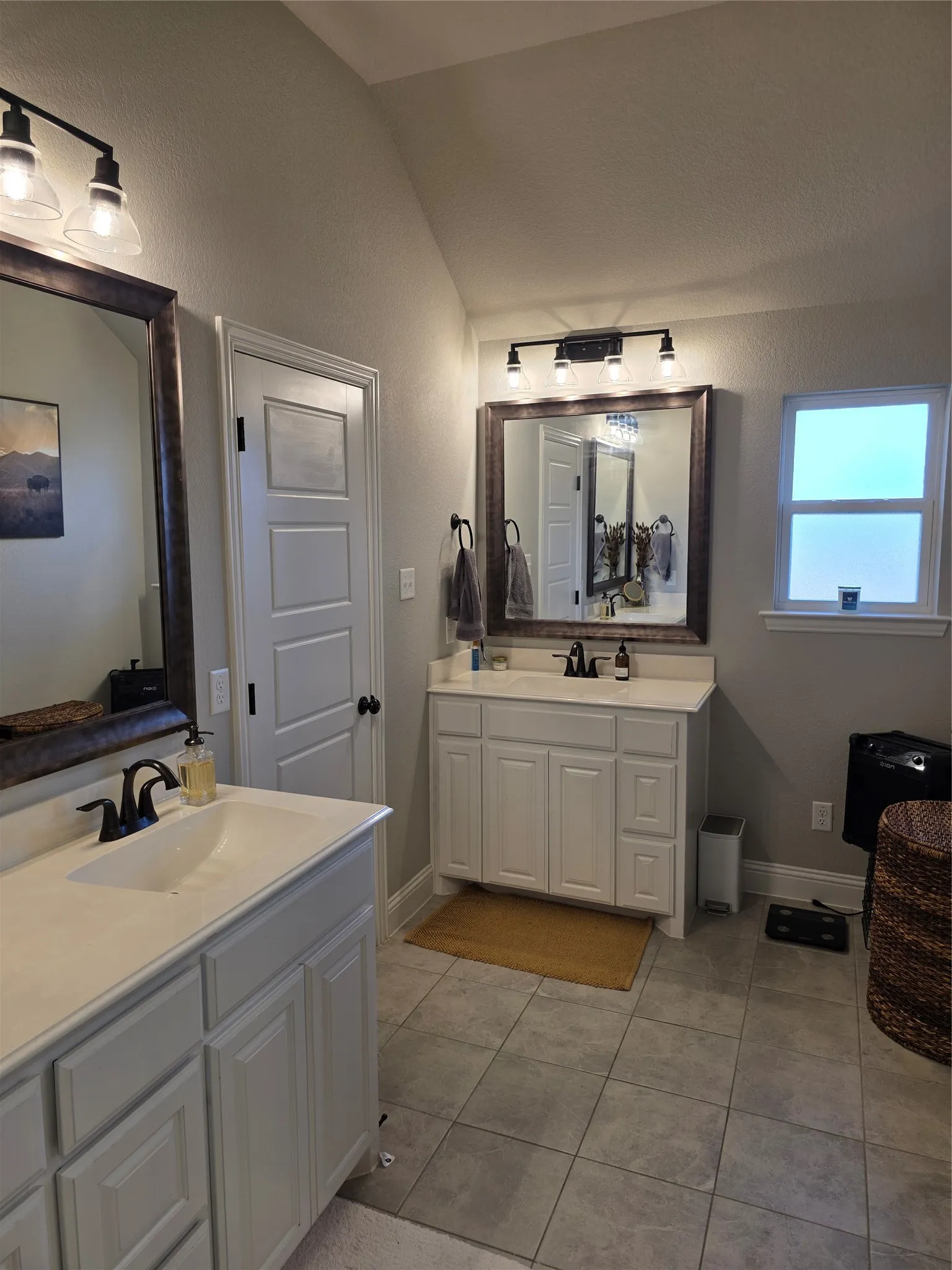 Bathroom with vaulted ceiling, two vanities, and light tile patterned floors
