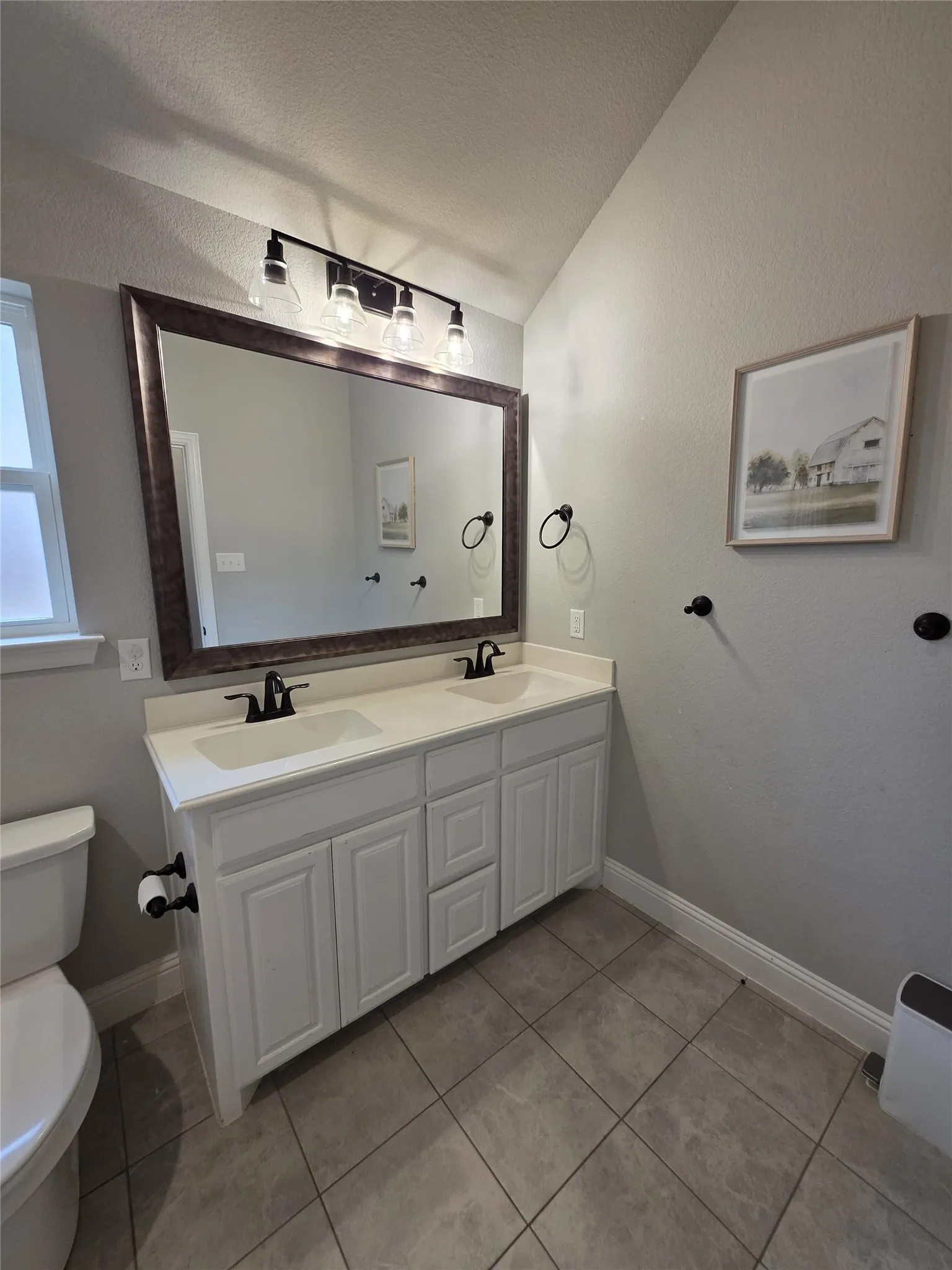 Bathroom featuring vaulted ceiling, double vanity, and light tile patterned floors