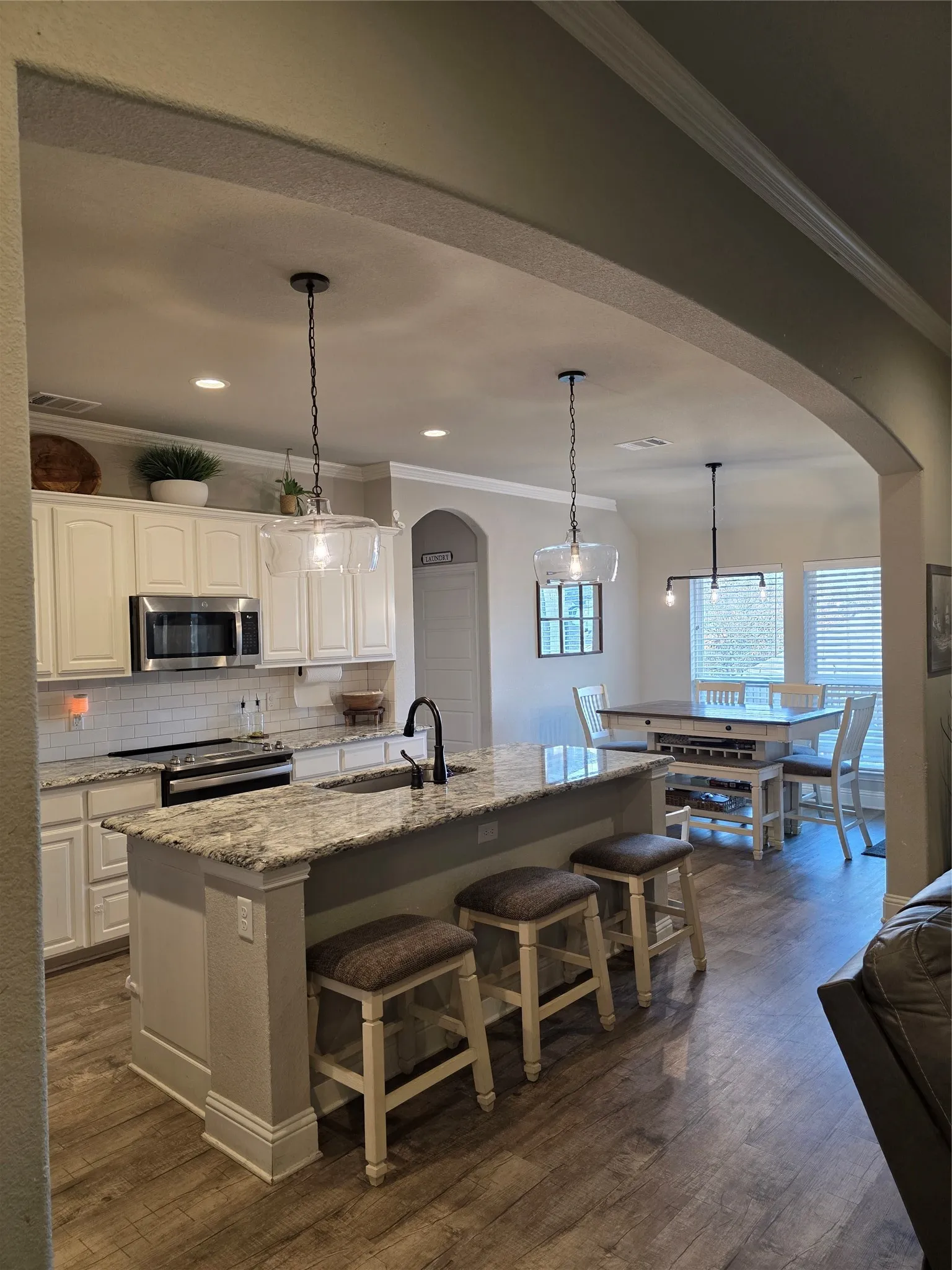 Kitchen featuring arched walkways, pendant lighting, crown molding, light stone countertops, and appliances with stainless steel finishes