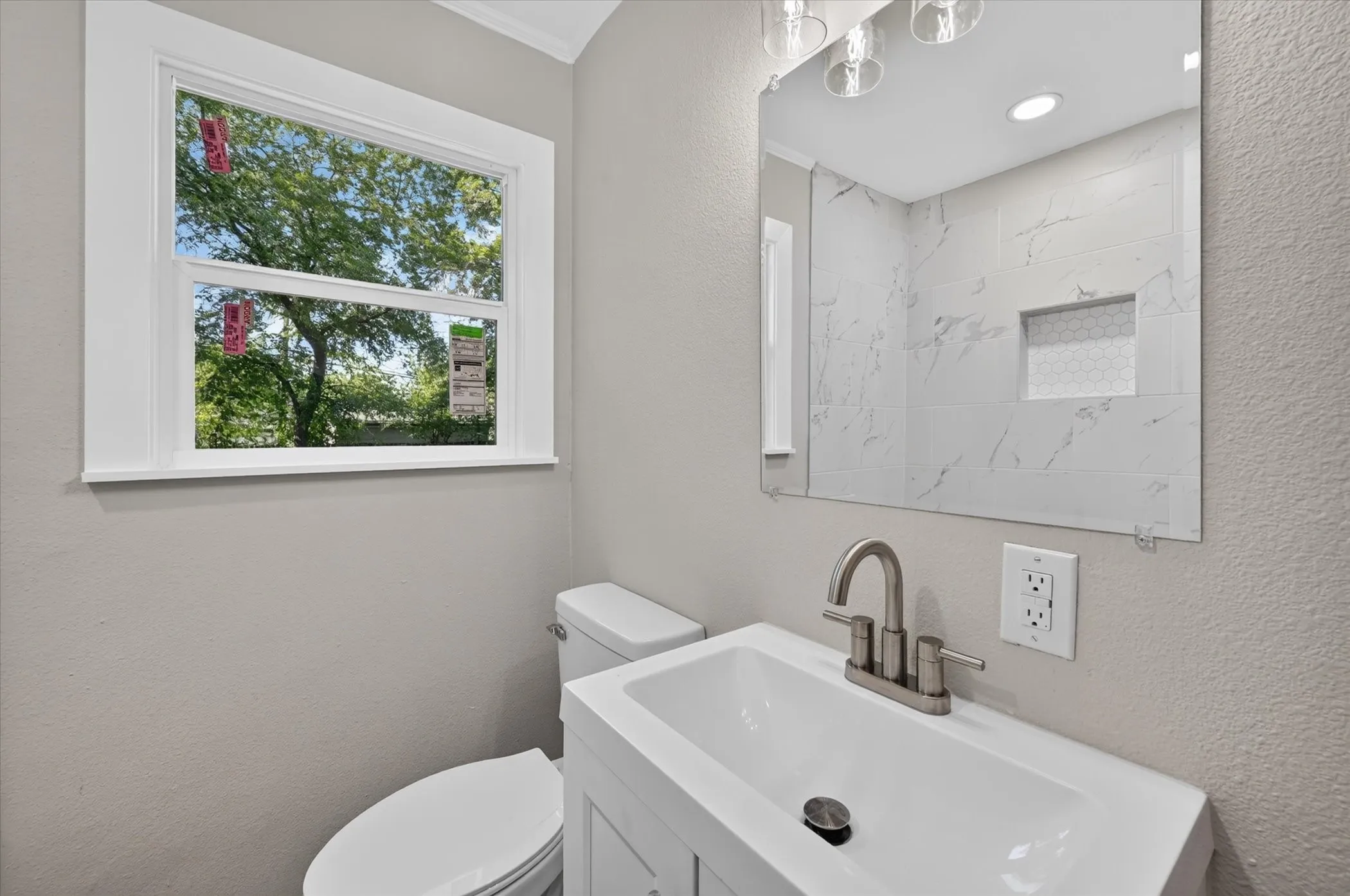 White vanity with integrated sink, brushed nickel faucet, large wall mirror, and tiled shower with recessed niche