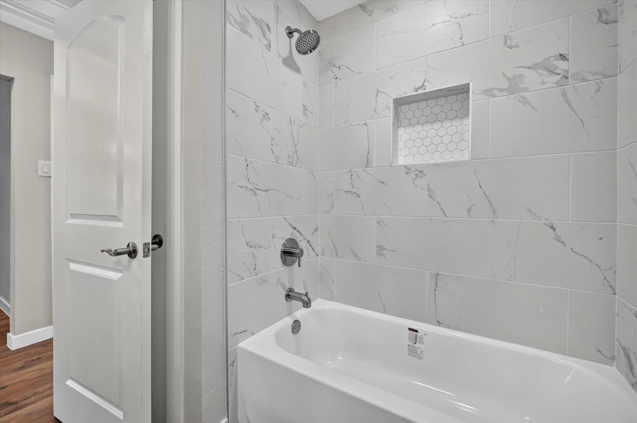 White vanity with integrated sink, brushed nickel faucet, large wall mirror, and tiled shower with recessed niche