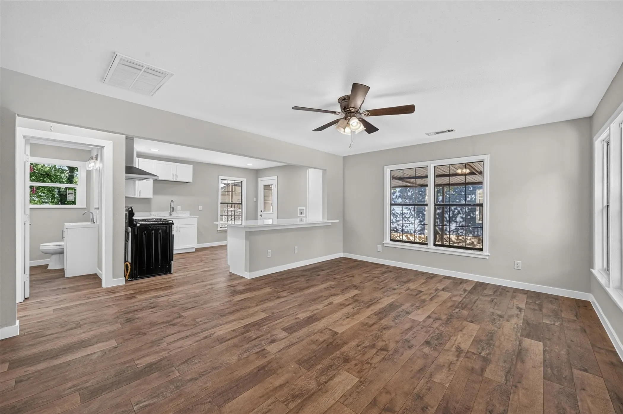 Open-concept living space featuring wood-finish flooring, a ceiling fan, and large windows
