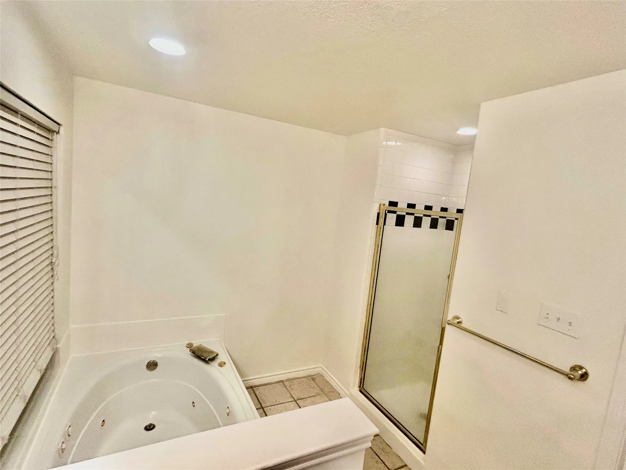 Jetted soaking tub with a tiled surround, adjacent to a shower with a glass enclosure and subway tile detailing