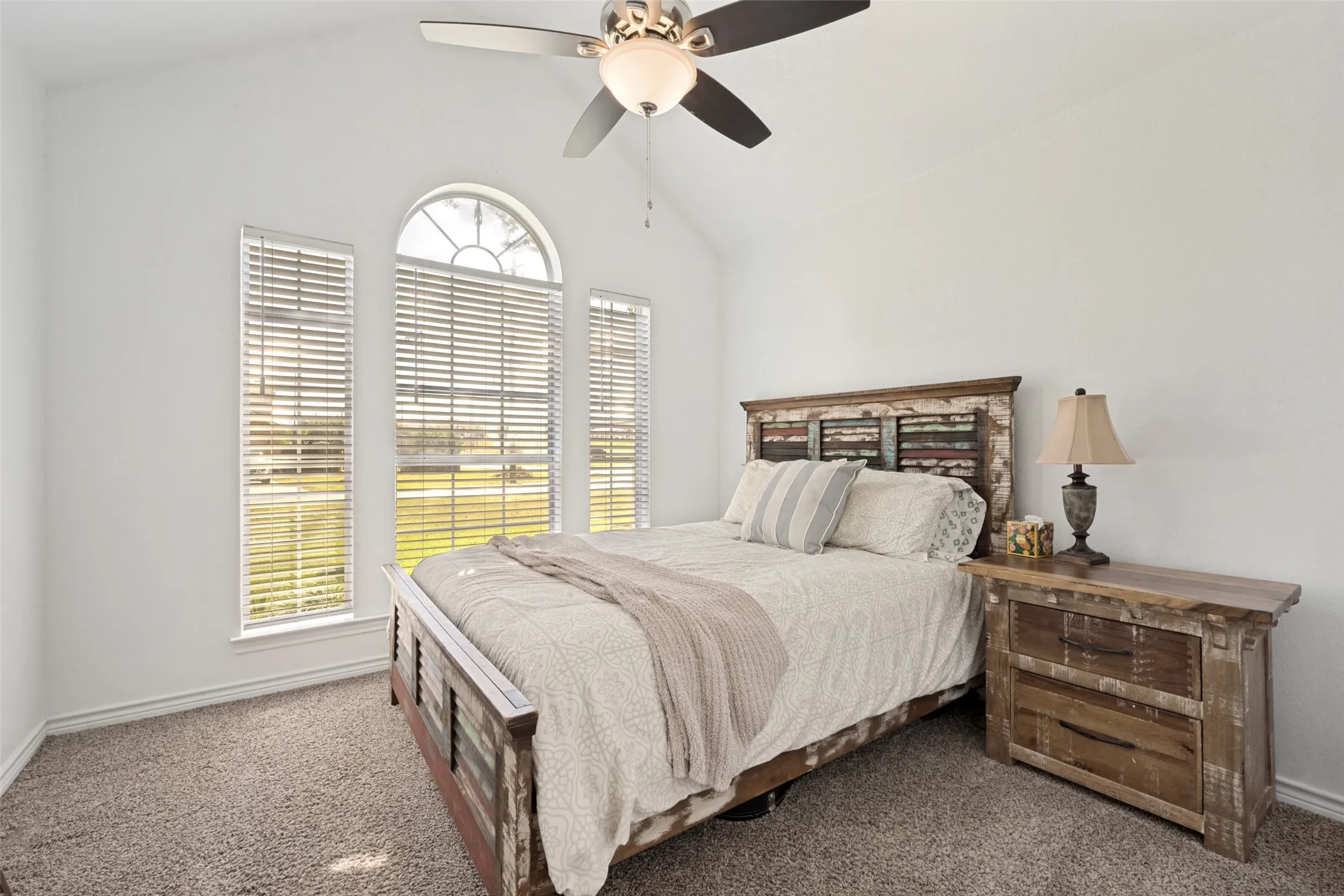 Vaulted ceilings with a ceiling fan, arched window, two vertical windows, and carpet flooring