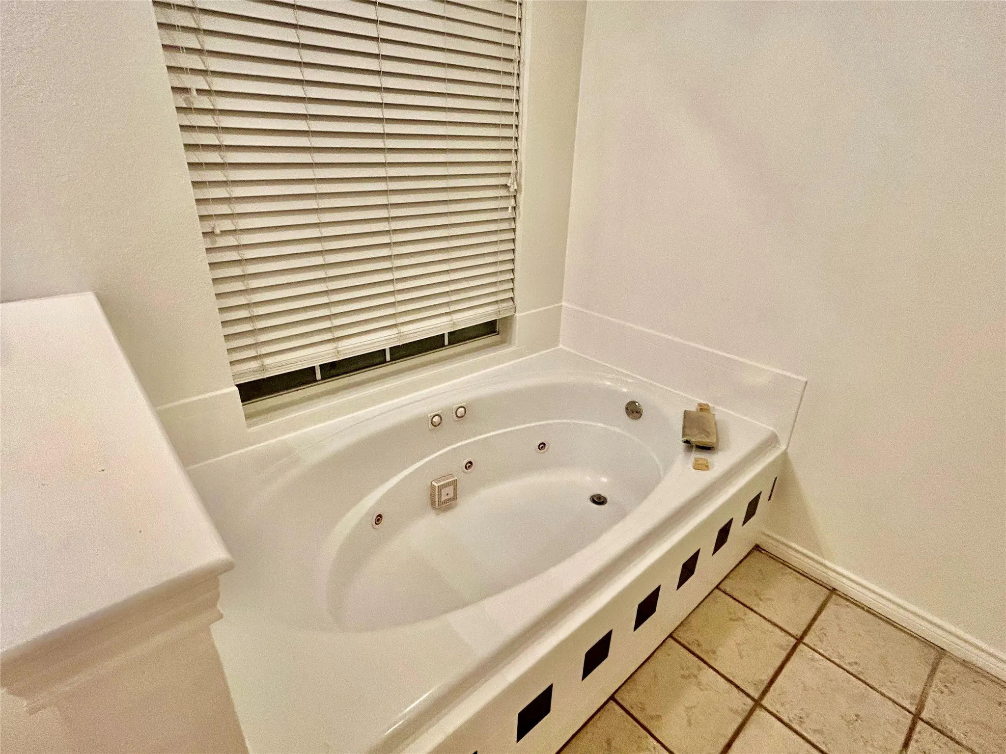 Corner jetted tub with tiled surround, a privacy window, and tiled flooring