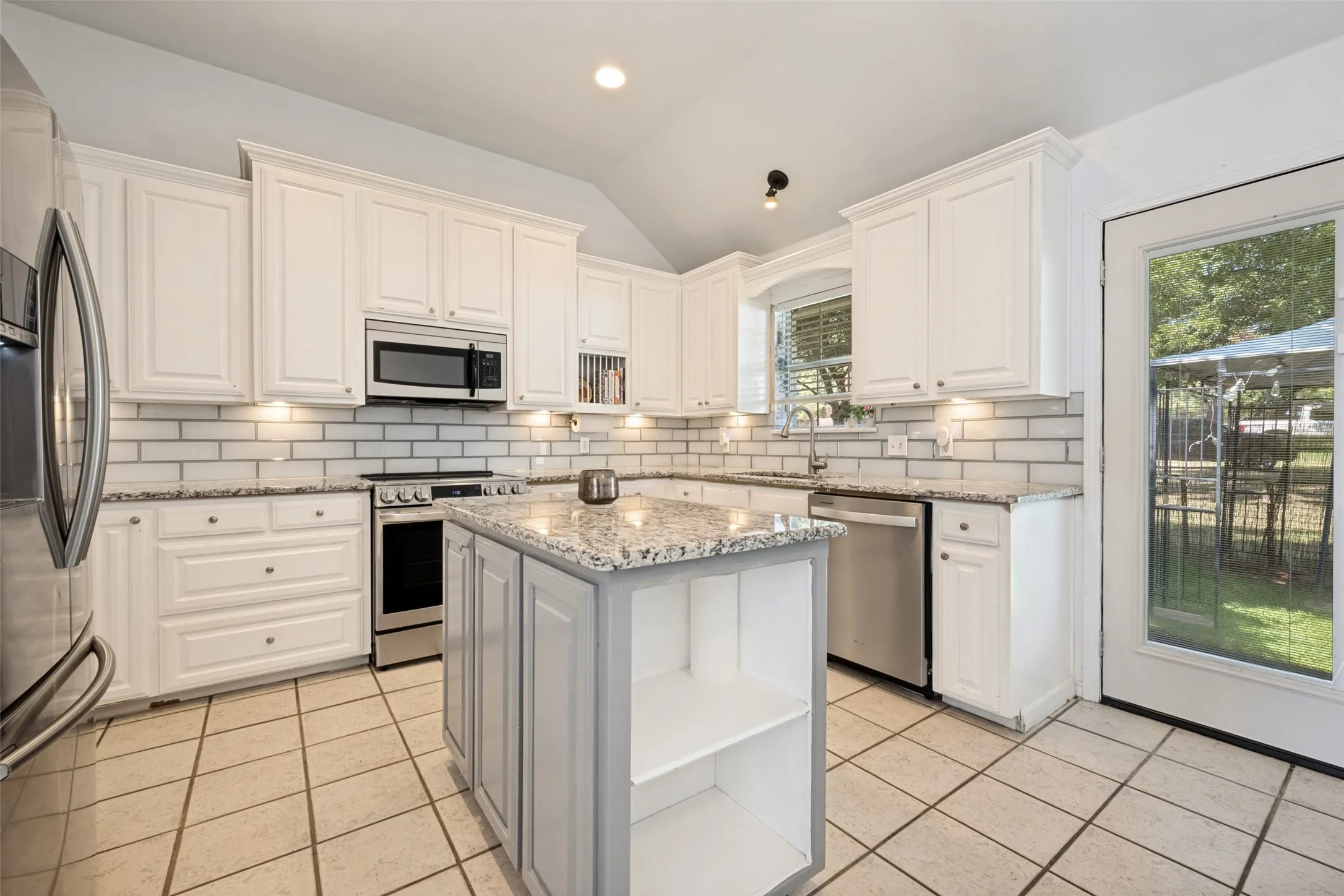 Kitchen featuring white cabinetry, subway tile backsplash, stainless steel appliances, granite countertops, and tile flooring