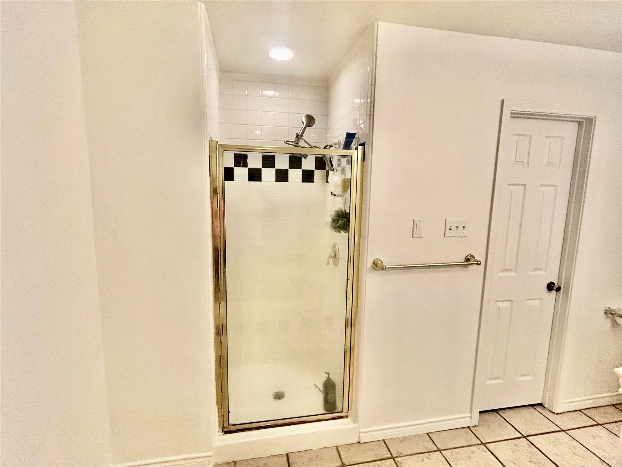 Shower enclosure with gold-tone framing, white subway tile surround, and checkerboard accent tile