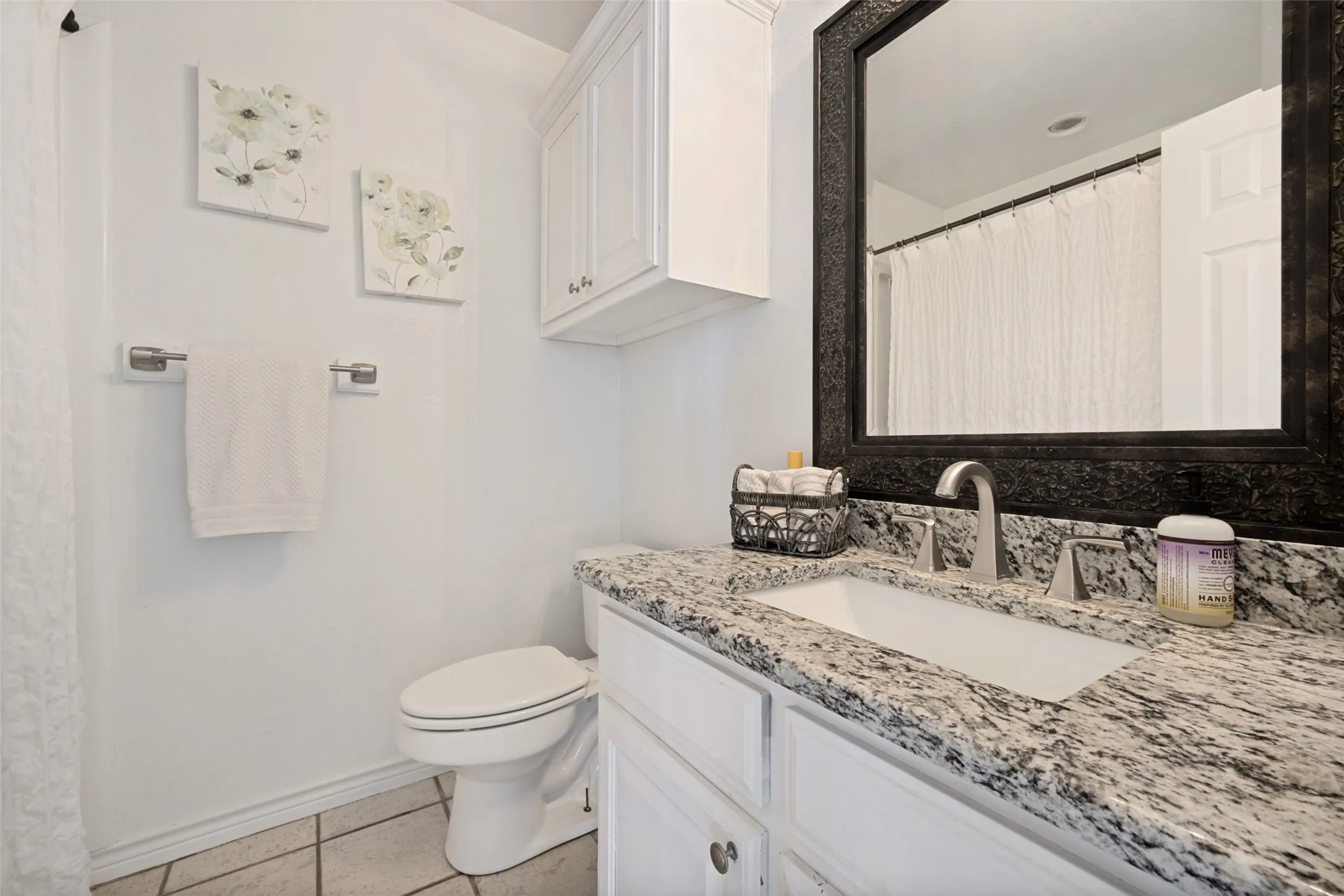 White vanity with a rectangular undermount sink, a gray speckled countertop, and a dark framed mirror