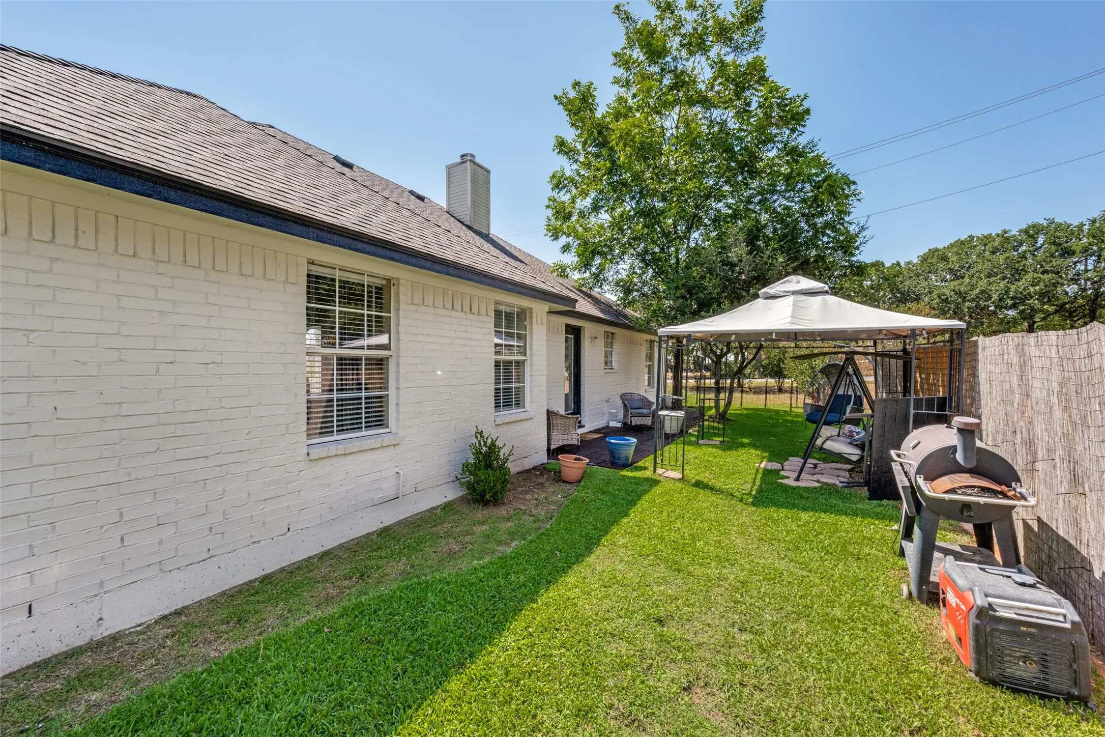 White brick exterior with a dark shingle roof and a covered patio area