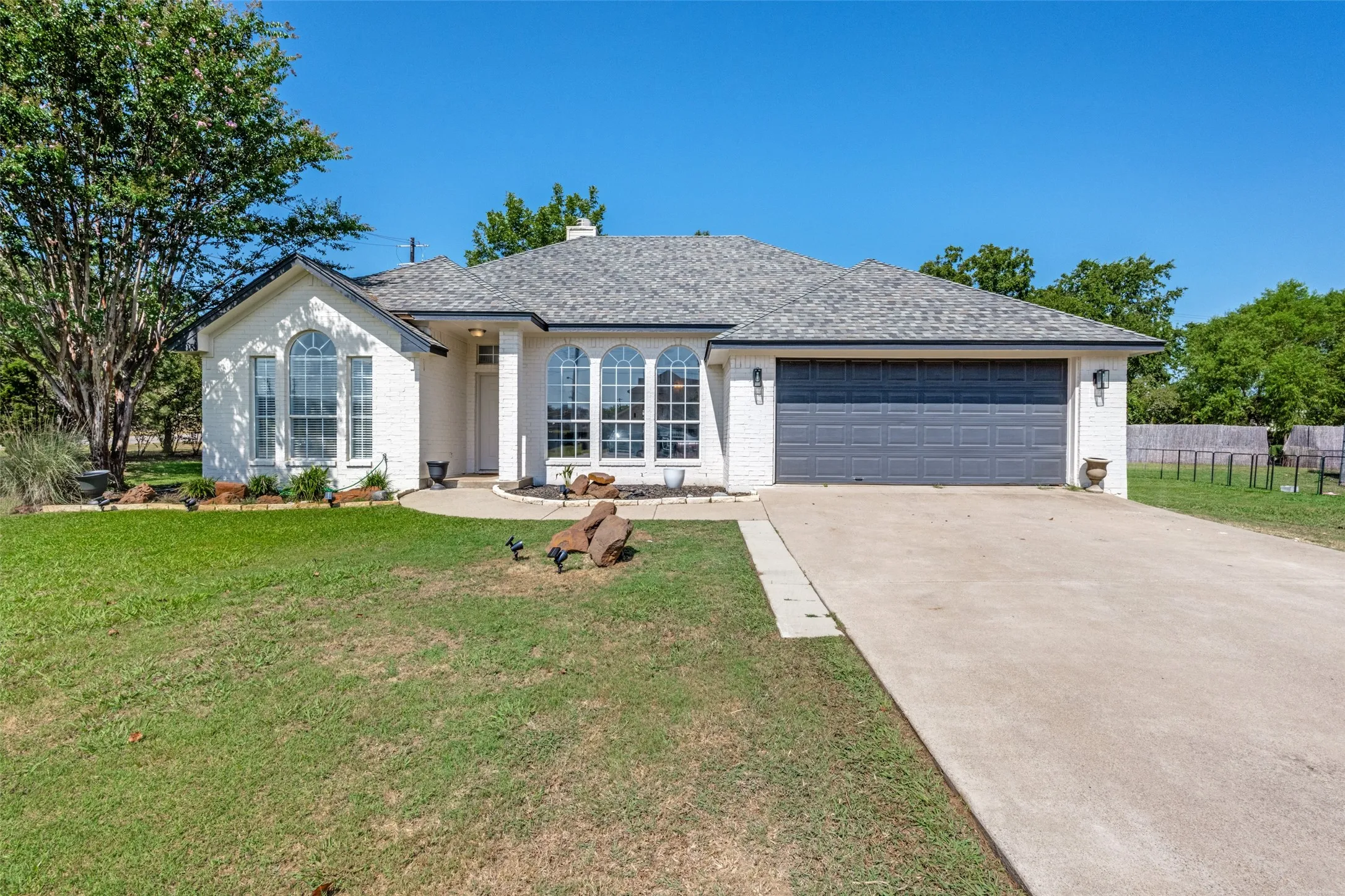 White stucco exterior, arched windows, attached garage, concrete driveway, and a shingled roof