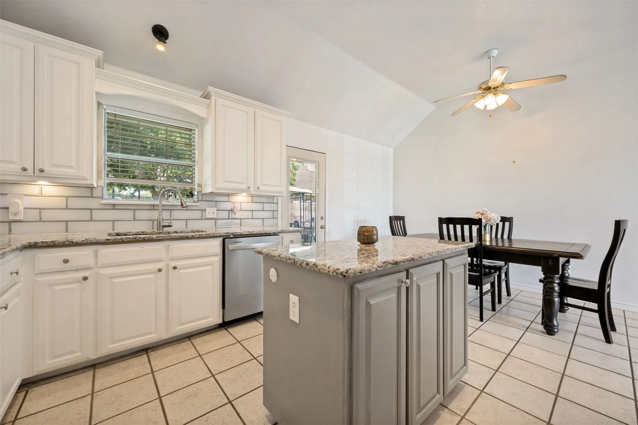 Kitchen featuring white shaker-style cabinetry, subway tile backsplash, stainless steel appliances, granite countertops, and a central island with storage