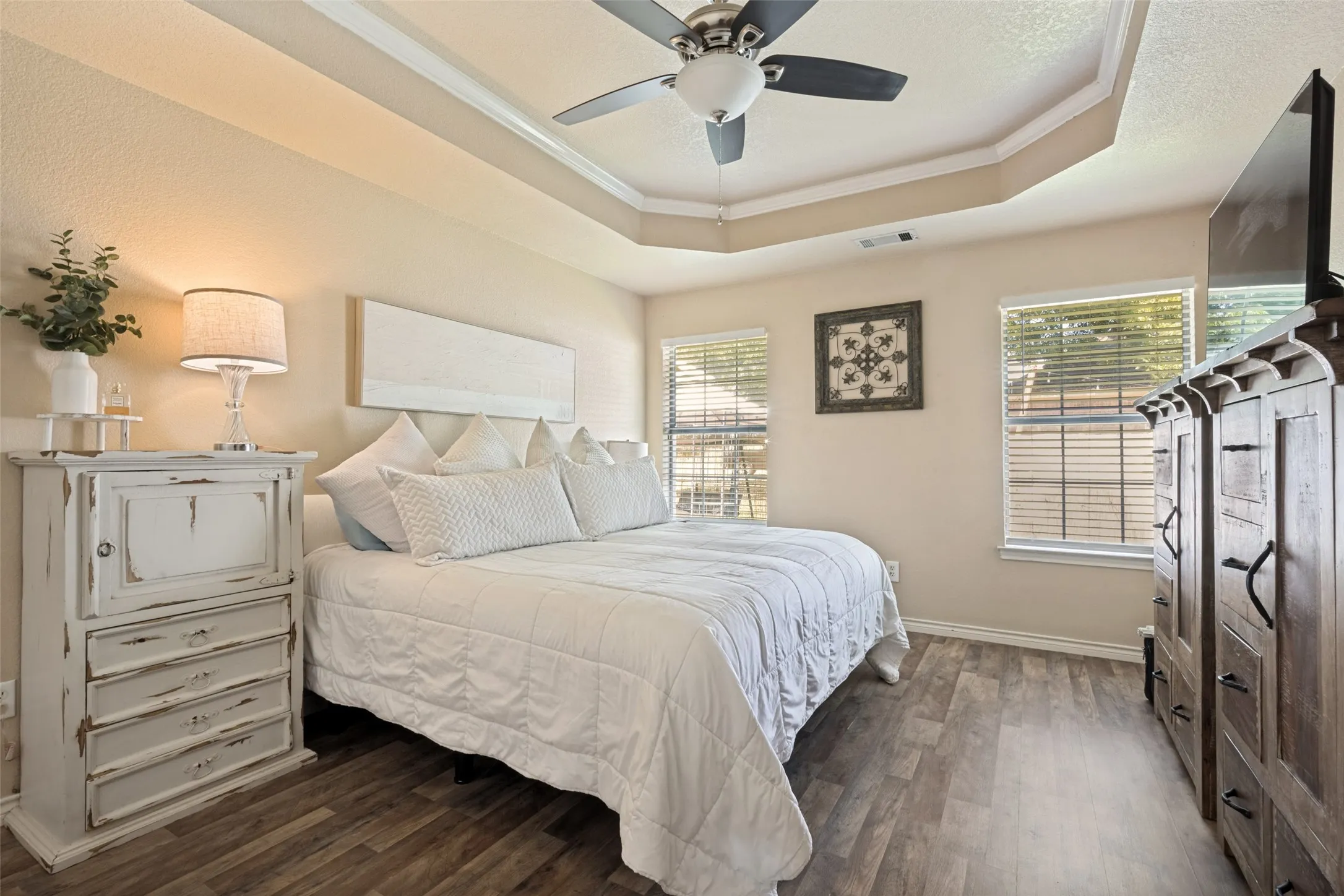 Wood-finish flooring, tray ceiling with crown molding, ceiling fan, and window blinds