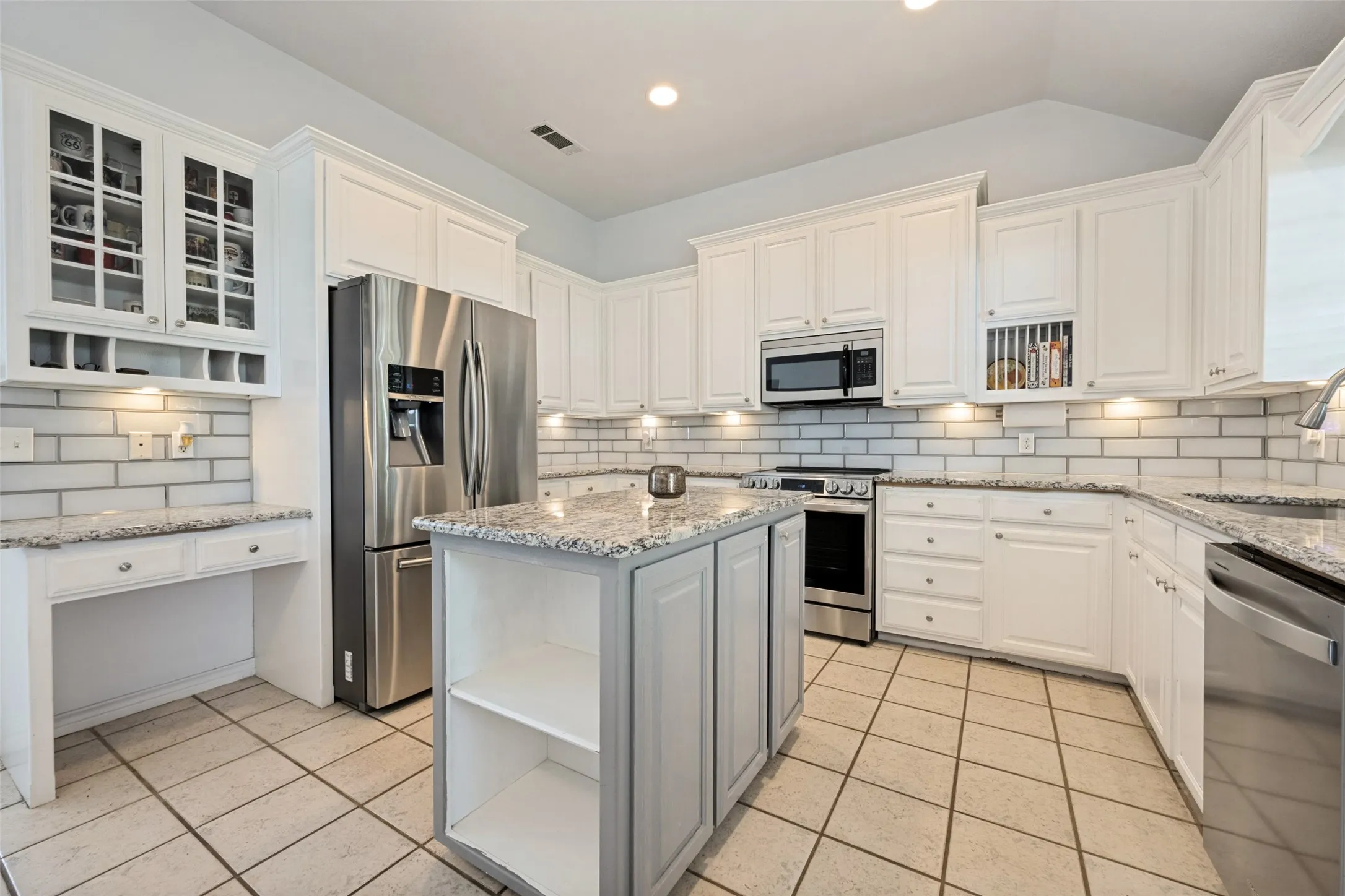 White cabinetry, granite countertops, subway tile backsplash, stainless steel appliances, and a central island with open shelving