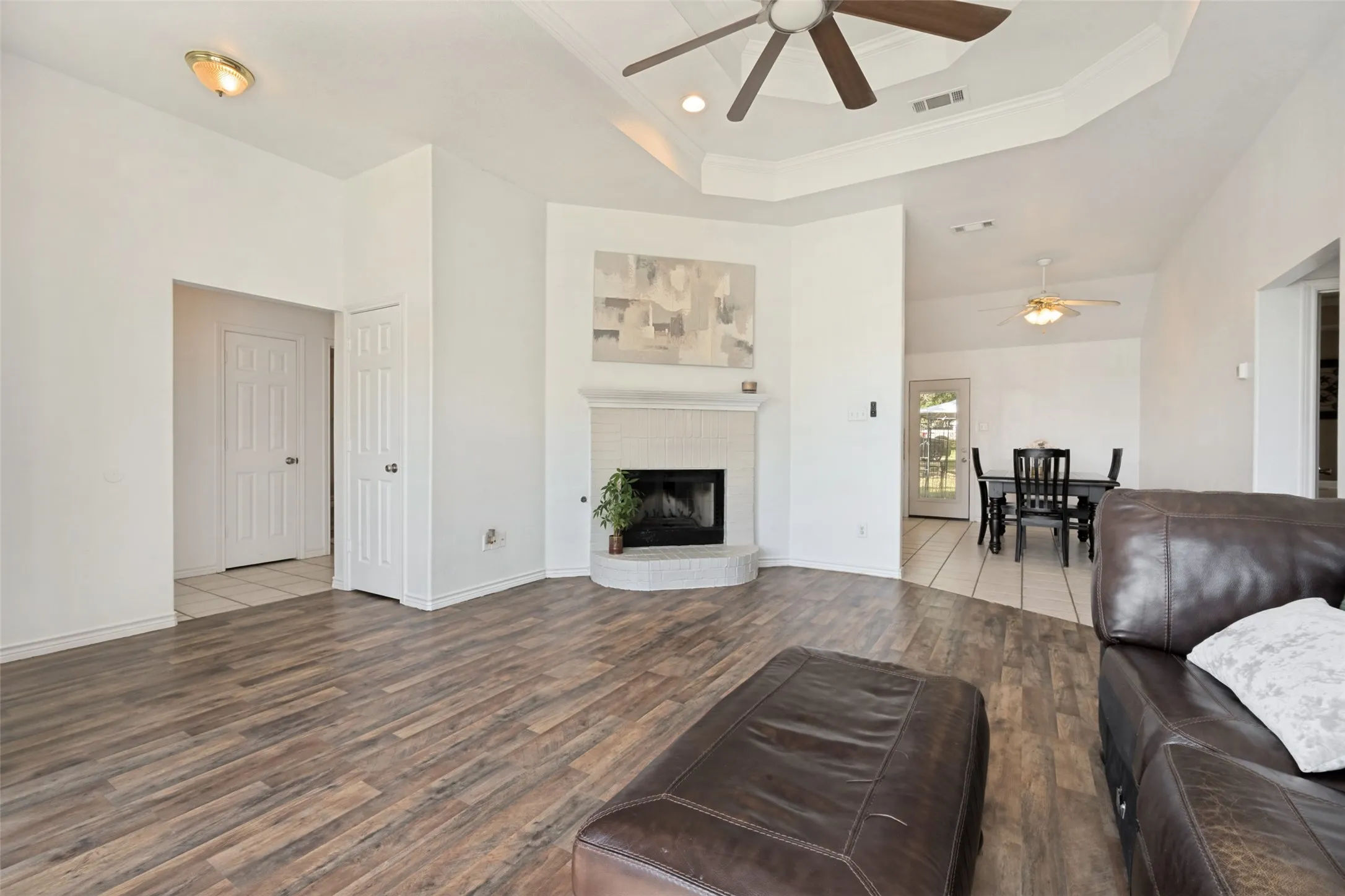Wood-finish flooring, white walls, tray ceiling with a ceiling fan, fireplace with a hearth, and built-in lighting