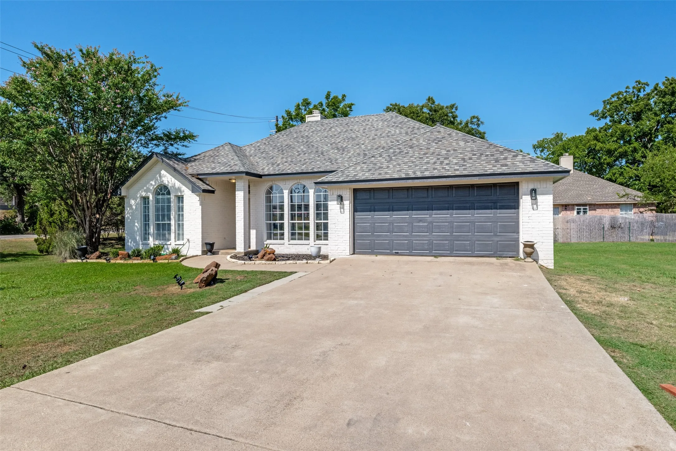 White brick exterior with a gray shingle roof, arched windows, and a two-car garage