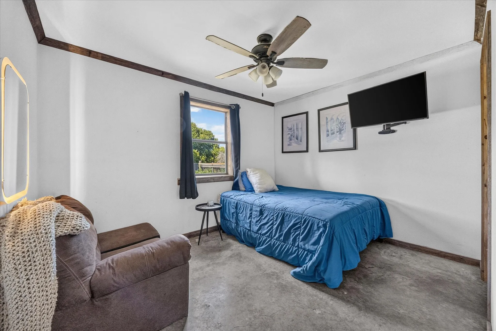 Ceiling fan light fixture, wood-finish ceiling trim, mounted wall television, window with outdoor scenery, and polished concrete flooring