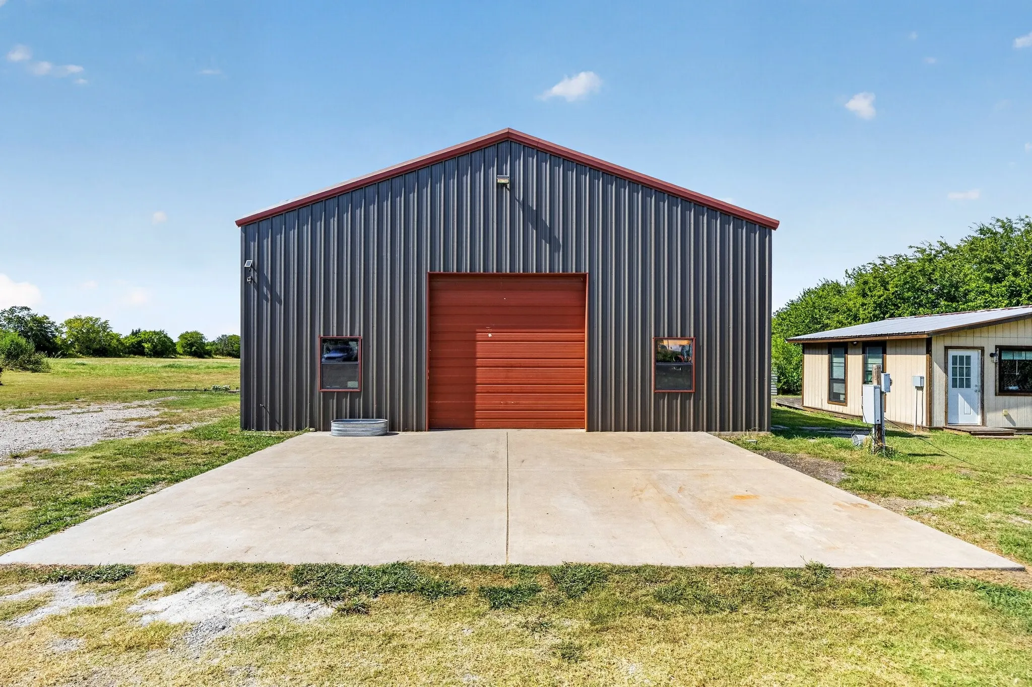 Metal-sided building featuring a red roll-up door, multiple windows, and a red-trimmed roof