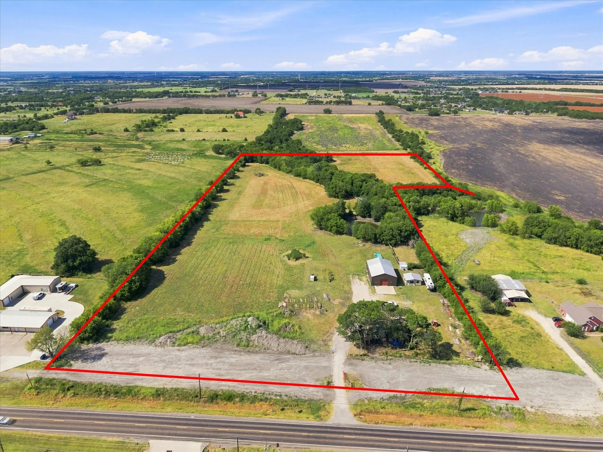 Expansive land parcel featuring a main structure, secondary building, gravel driveway, and surrounding green acreage with scattered trees