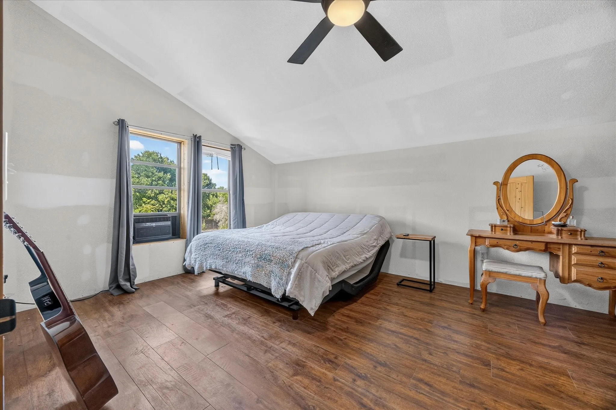 Room featuring wood-finish flooring, an angled ceiling, two windows, and a ceiling fan