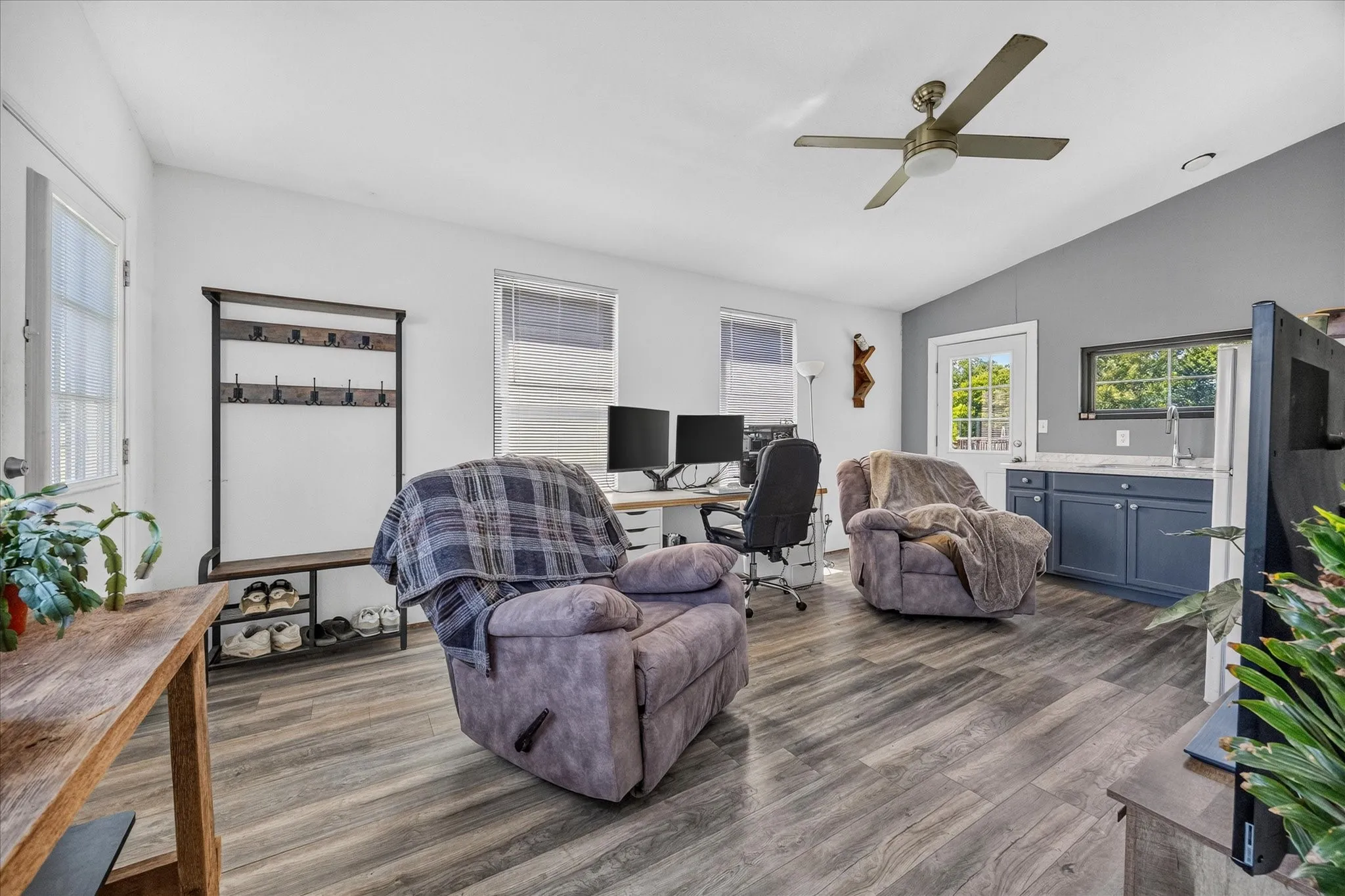 Wood-finish flooring throughout, a vaulted ceiling with a ceiling fan, and a built-in wet bar with a single basin sink and blue cabinetry