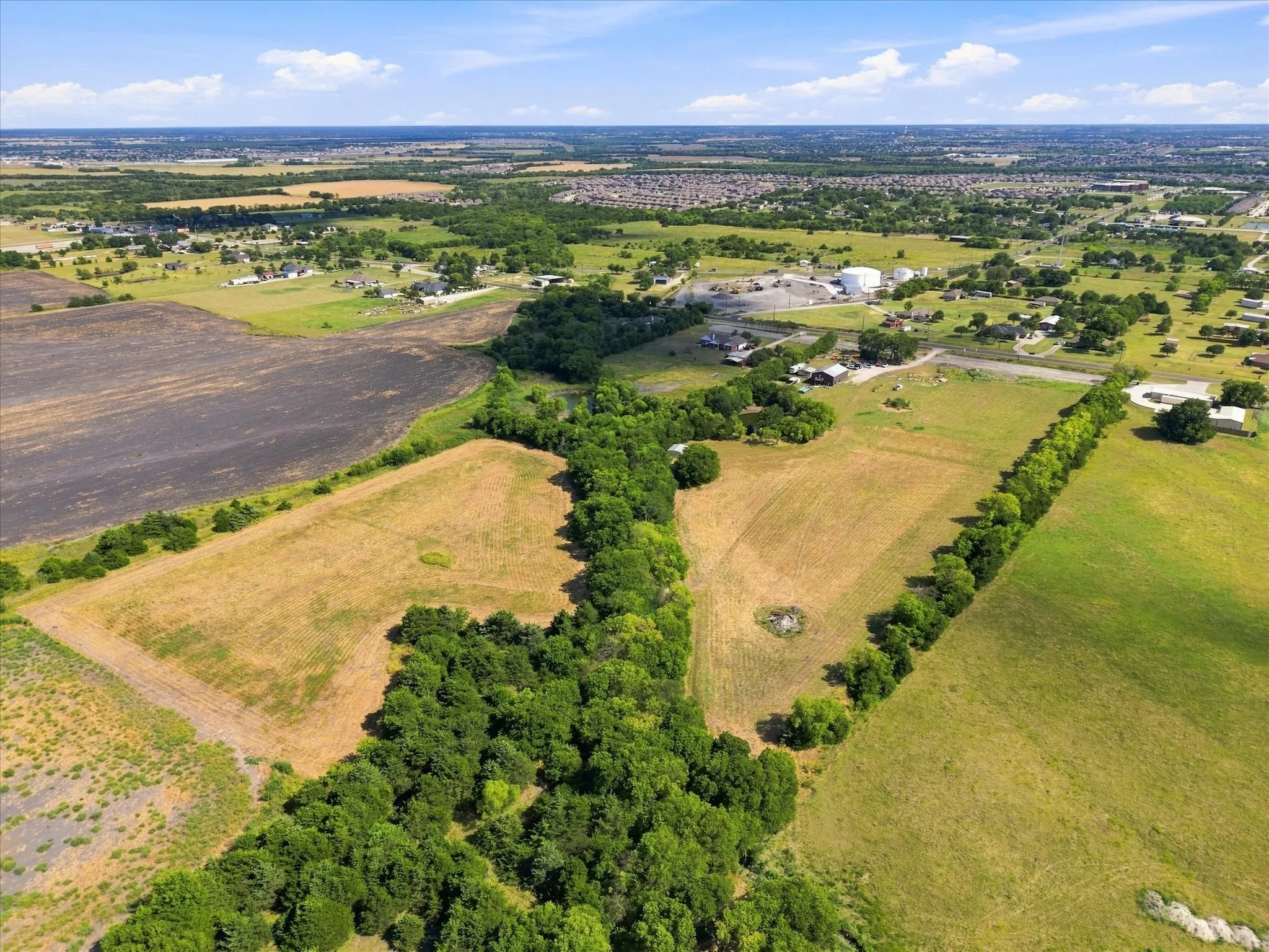Expansive land parcel featuring open fields, wooded sections, and distant structures