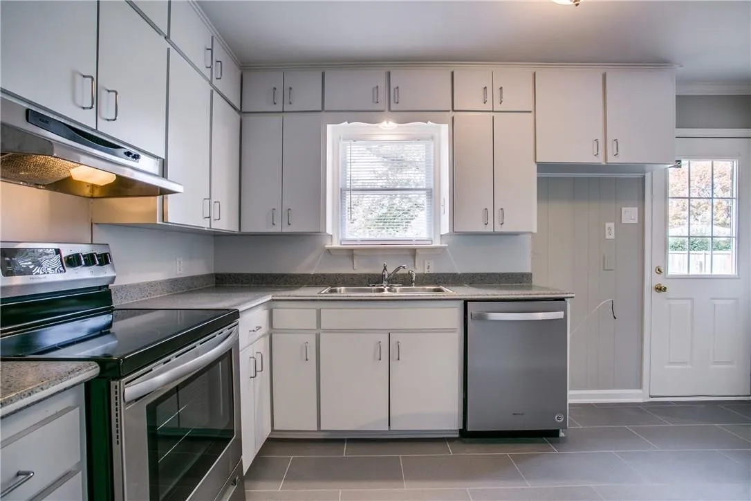 Kitchen featuring extensive white cabinetry, stainless steel appliances, a double basin sink, and ample countertop space