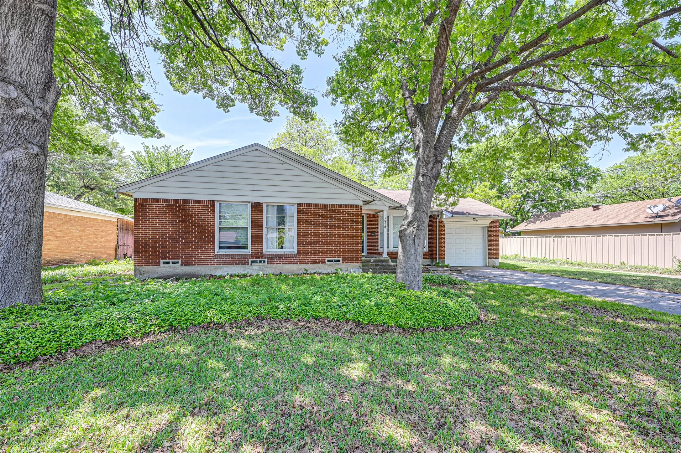 Brick exterior, pitched gable roof, attached garage, mature trees, and a concrete driveway