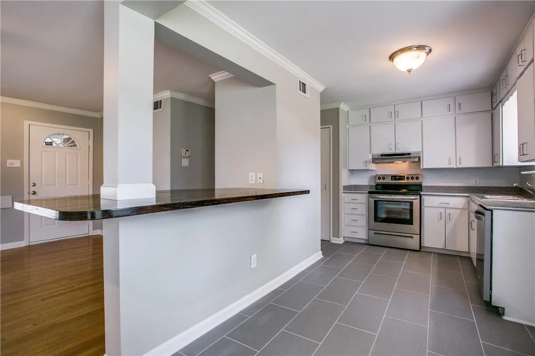 Kitchen featuring white cabinetry, stainless steel appliances, dark stone countertops, and gray tile flooring