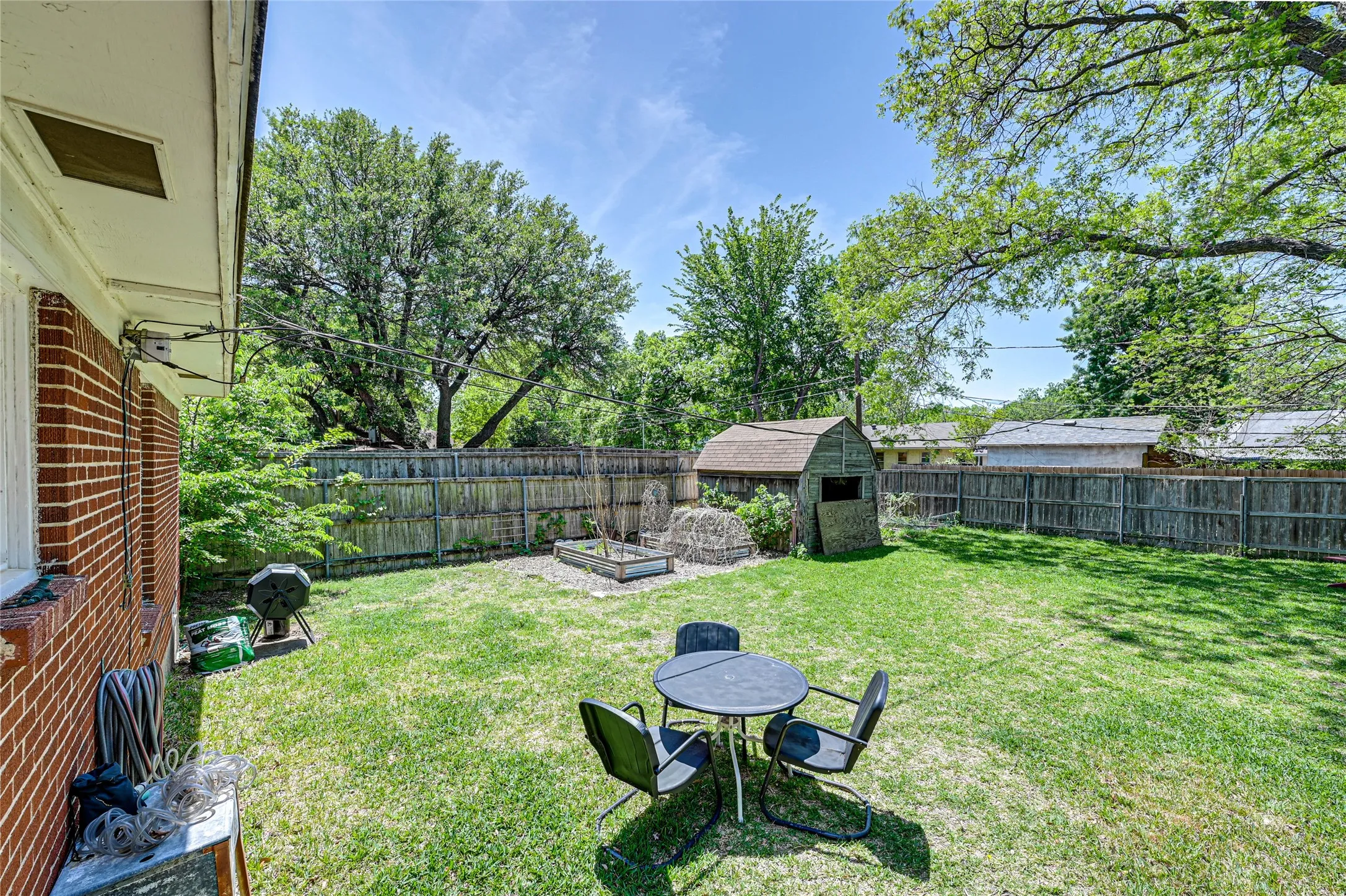 Expansive fenced backyard featuring a grassy lawn, a storage shed, and a raised garden bed
