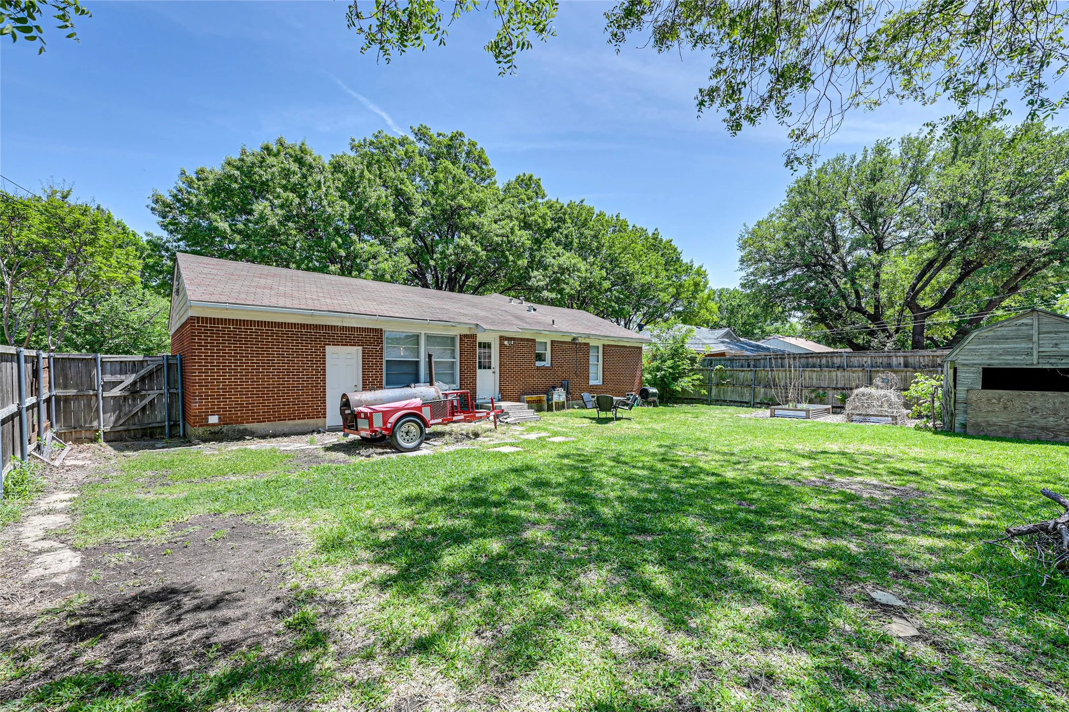 Expansive backyard featuring a brick exterior, shingle roof, wood privacy fencing, and a detached storage shed
