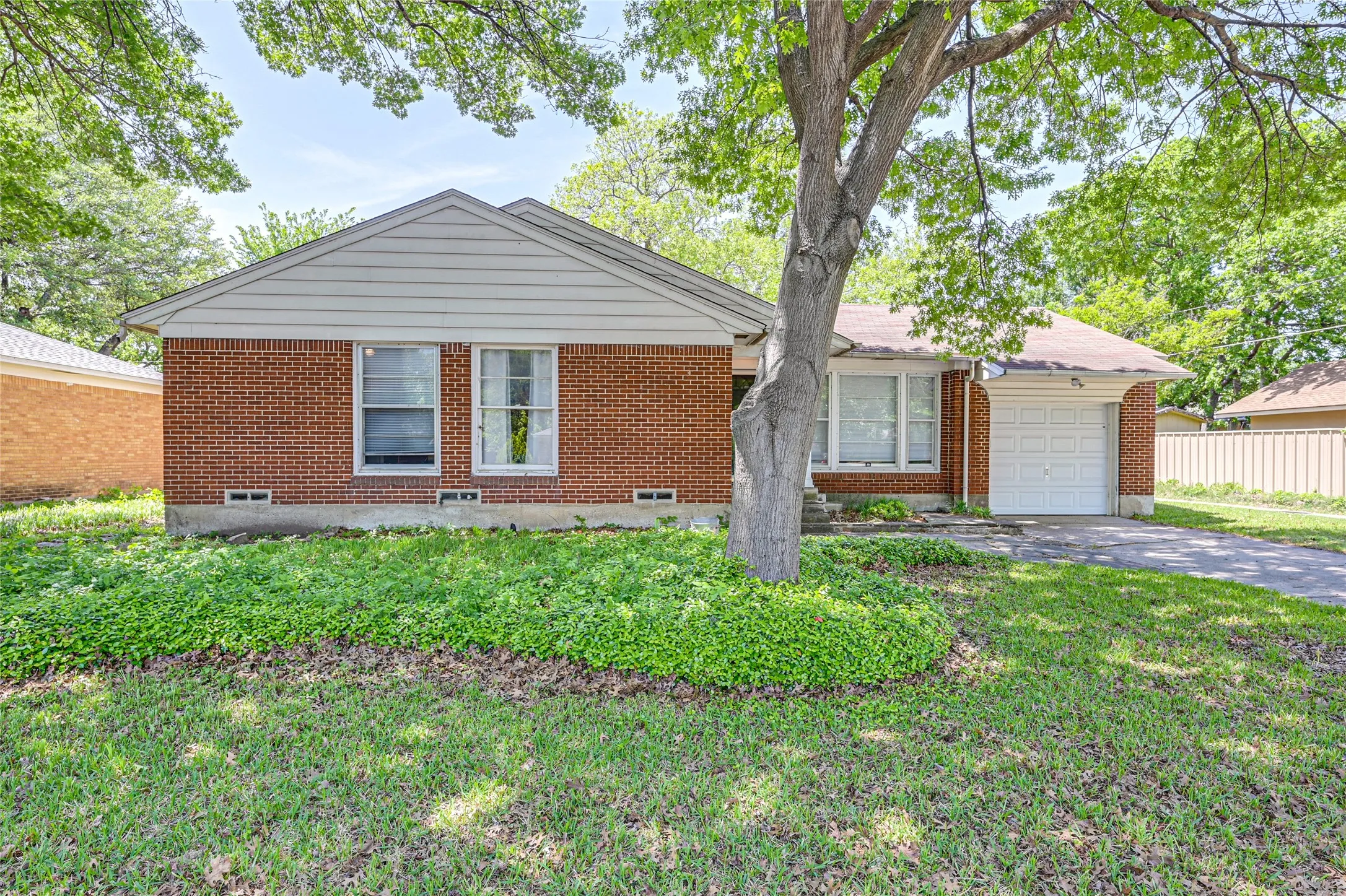 Brick exterior, single-car garage, mature trees, front yard with established plantings, paved driveway