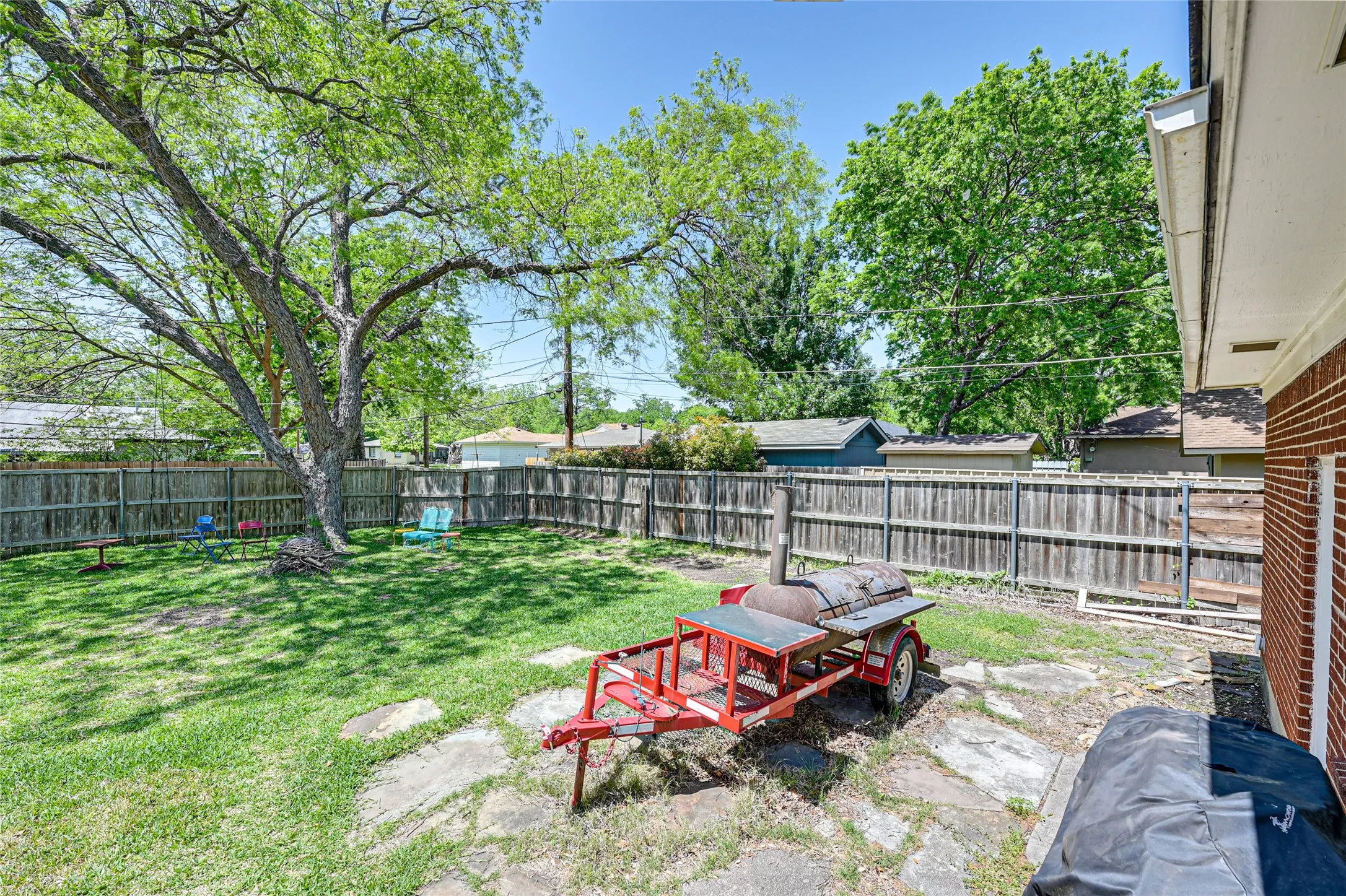 Expansive backyard with a manicured lawn, mature shade tree, full privacy fencing, and a stone patio